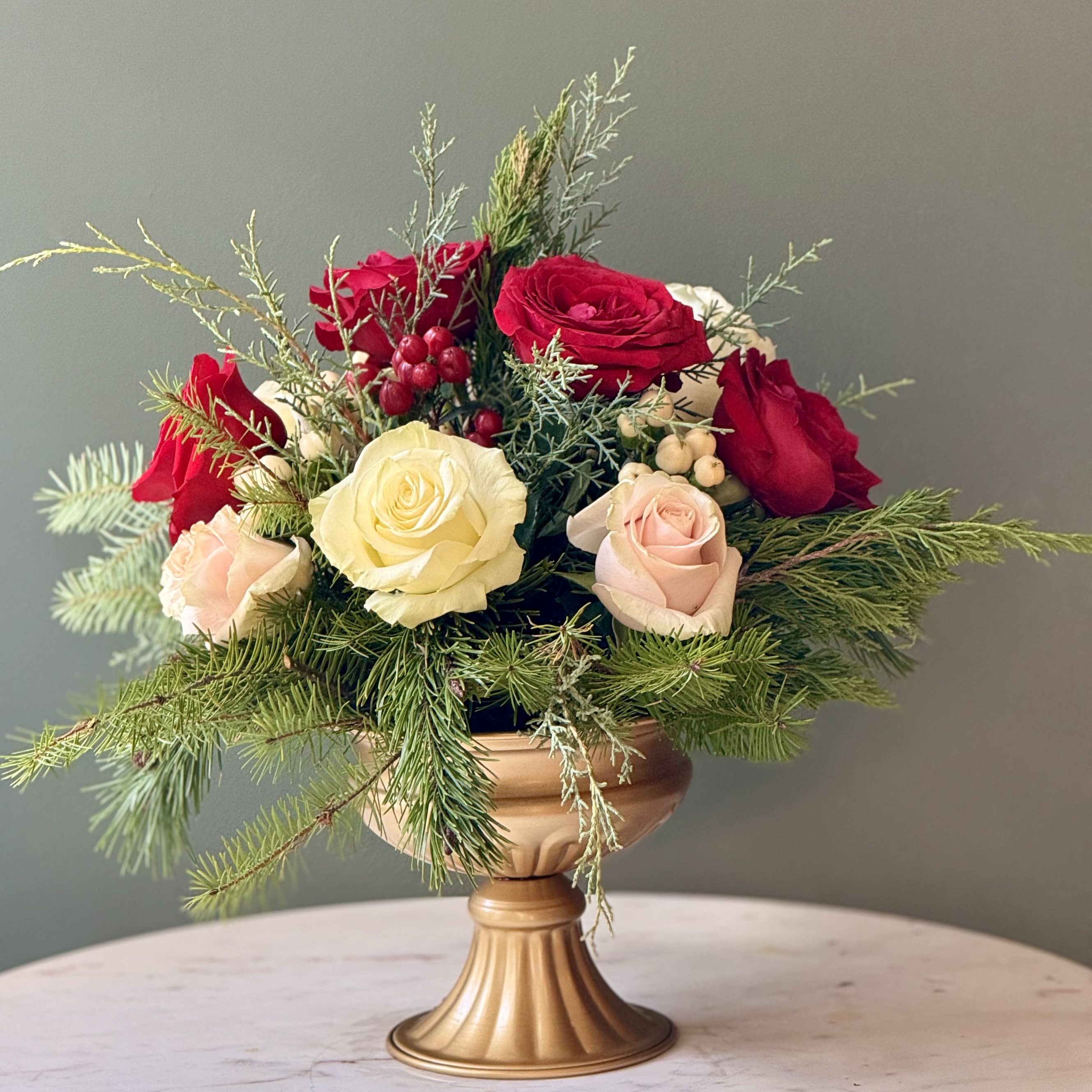 Winter Blooms - A sophisticated winter floral design for moments that deserve a touch of elegance this holiday season. Featuring: - Ecuadorian Roses - Hypericum - Styled with premium seasonal foliage Presentation Options: White urn Every order includes: A custom message card - simply enter your message at checkout and we'll take care of the rest. Please note: Flowers are subject to seasonal availability. If a listed flower is unavailable, our designers will substitute it with flowers of a similar shape, color, and style to maintain the overall aesthetic.