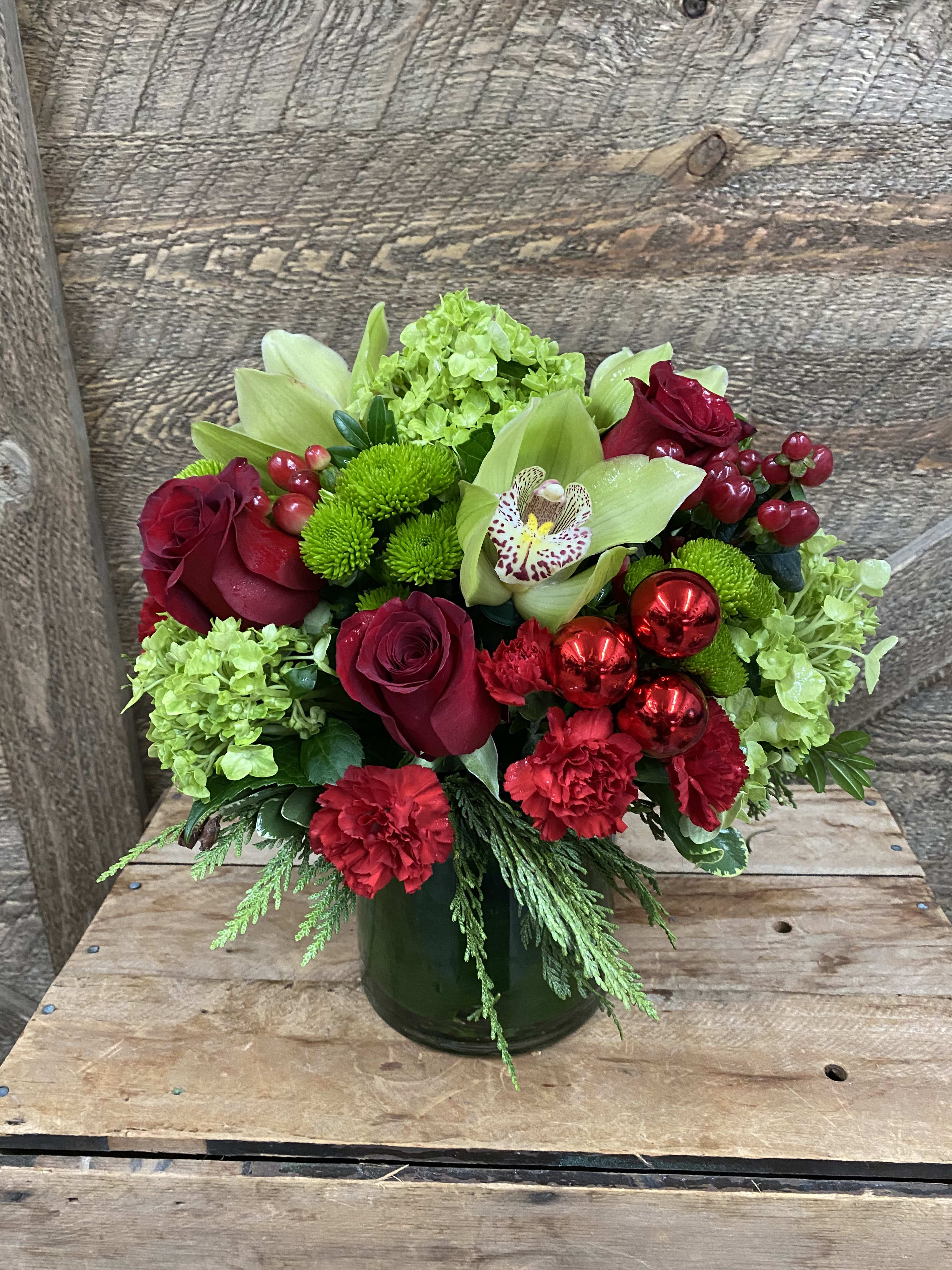 A Christmas to remember - A stunning design that includes green hydrangea, red roses, green cymbidium orchids,  hypericum berries, mini carnations, mums and evergreens. Arrangement is designed in a clear glass leafed wrapped vase. 