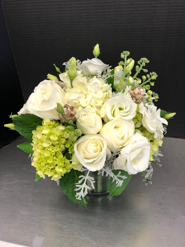 Winter Wonderland - This classy all white arrangement includes hydrangea, roses, lisianthus, dusty miller and pine cones. Arrangement is designed tight and tailored in a clear glass vase.