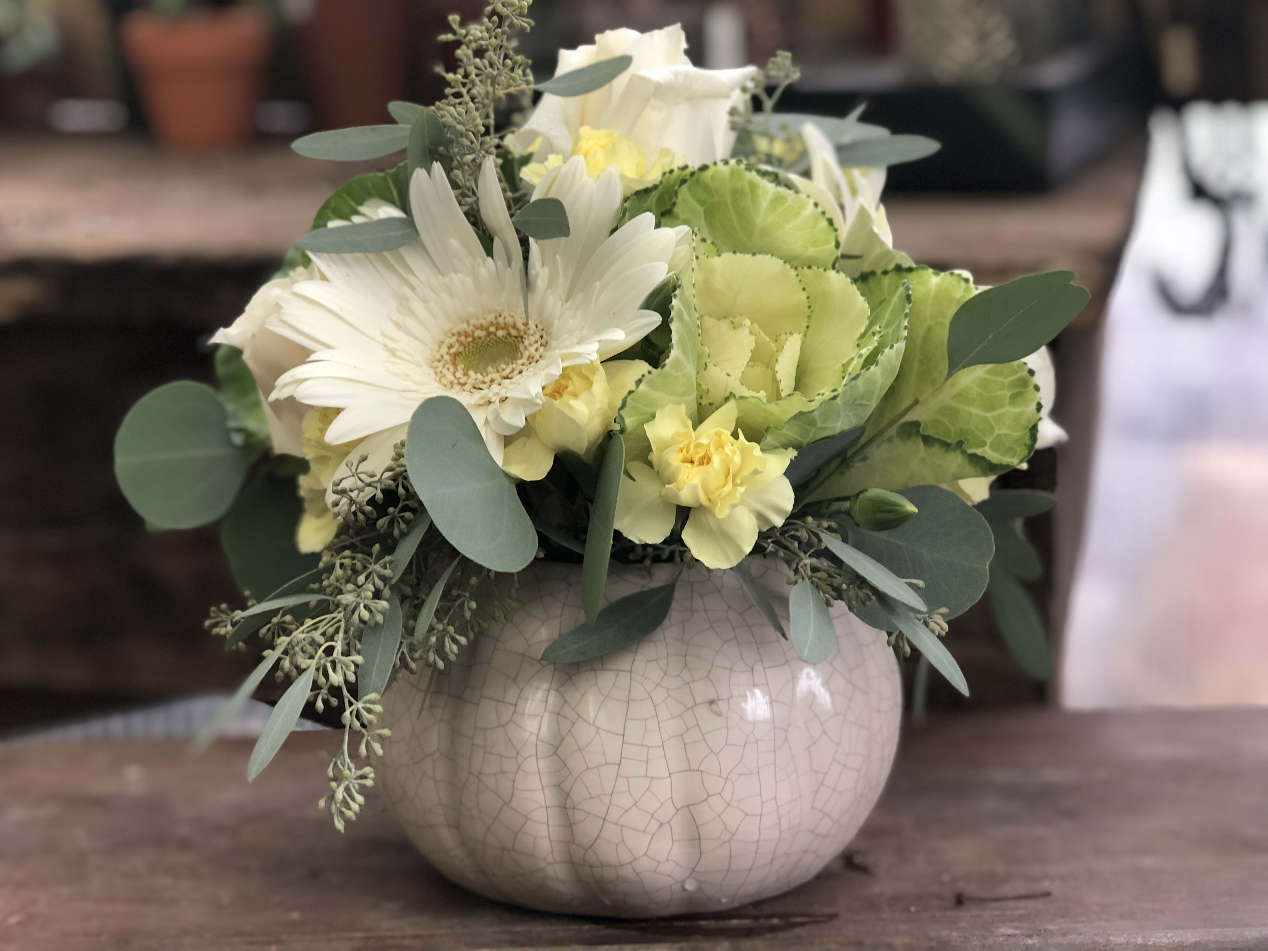 Spooktacular Blooms - A unique take on the typical fall pumpkin arrangement! This arrangement makes a statement with muted fall tones using Kale, Gerbs, Roses, Mini Carns and eucalpytus.  This reusable ceramic pumpkin is also a great seasonal decor item to bring our every year.  Get those heads turnin'!