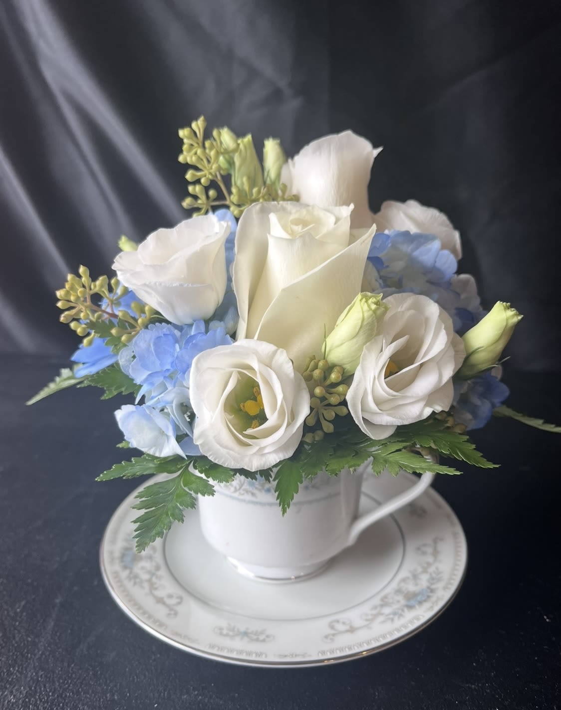 Blueberry Cream Tea Cup  - This adorable tea cup is made with light blue hydrangea , Roses, white Lisianthus and greenery. 
