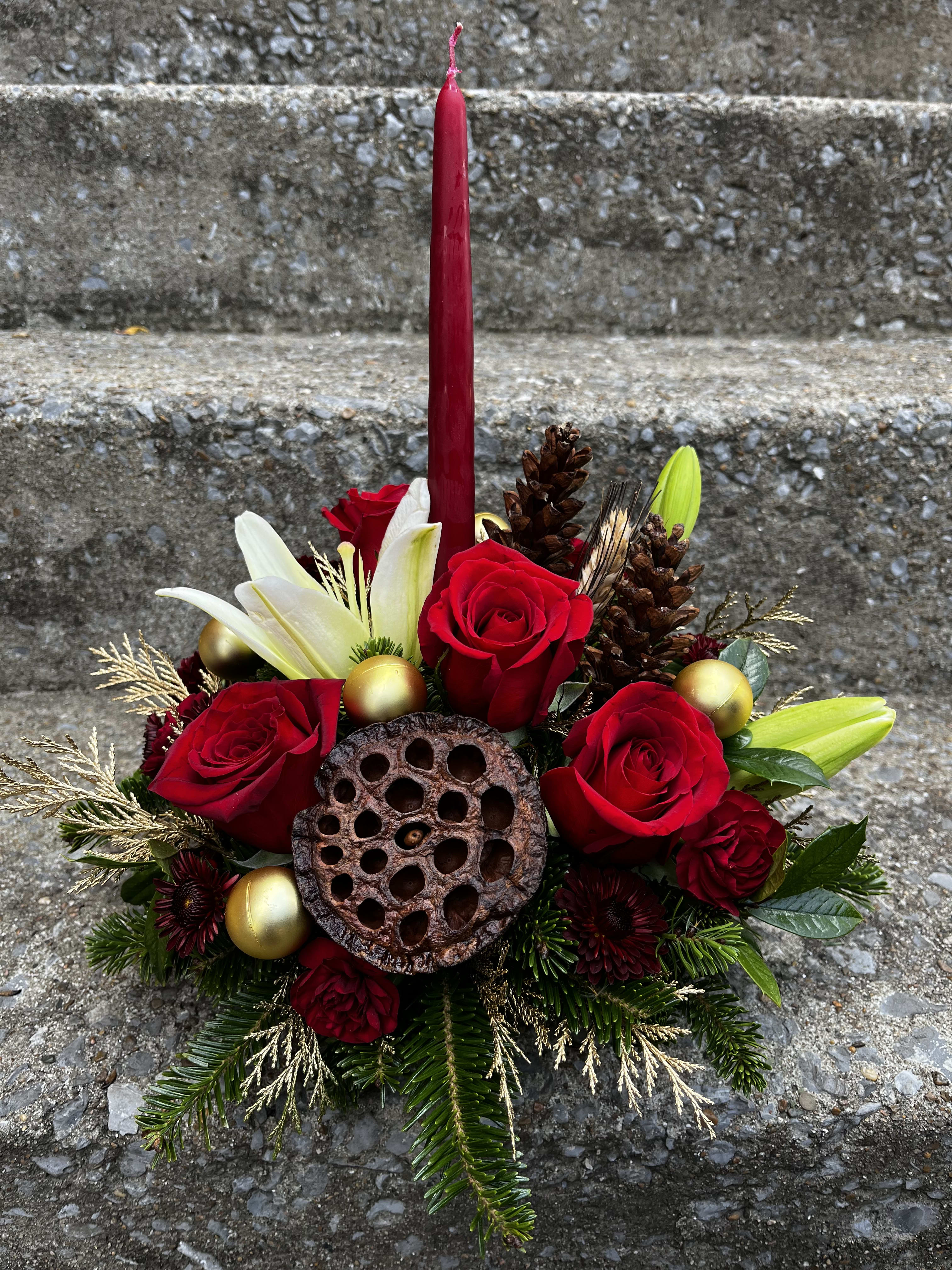 Christmas Cheer - This arrangement has roses, lilies, Christmas ornaments, pinecones, mums , mini carns, Christmas greens, golden, colored Christmas greens, a pod and a pomegranate colored red candle.