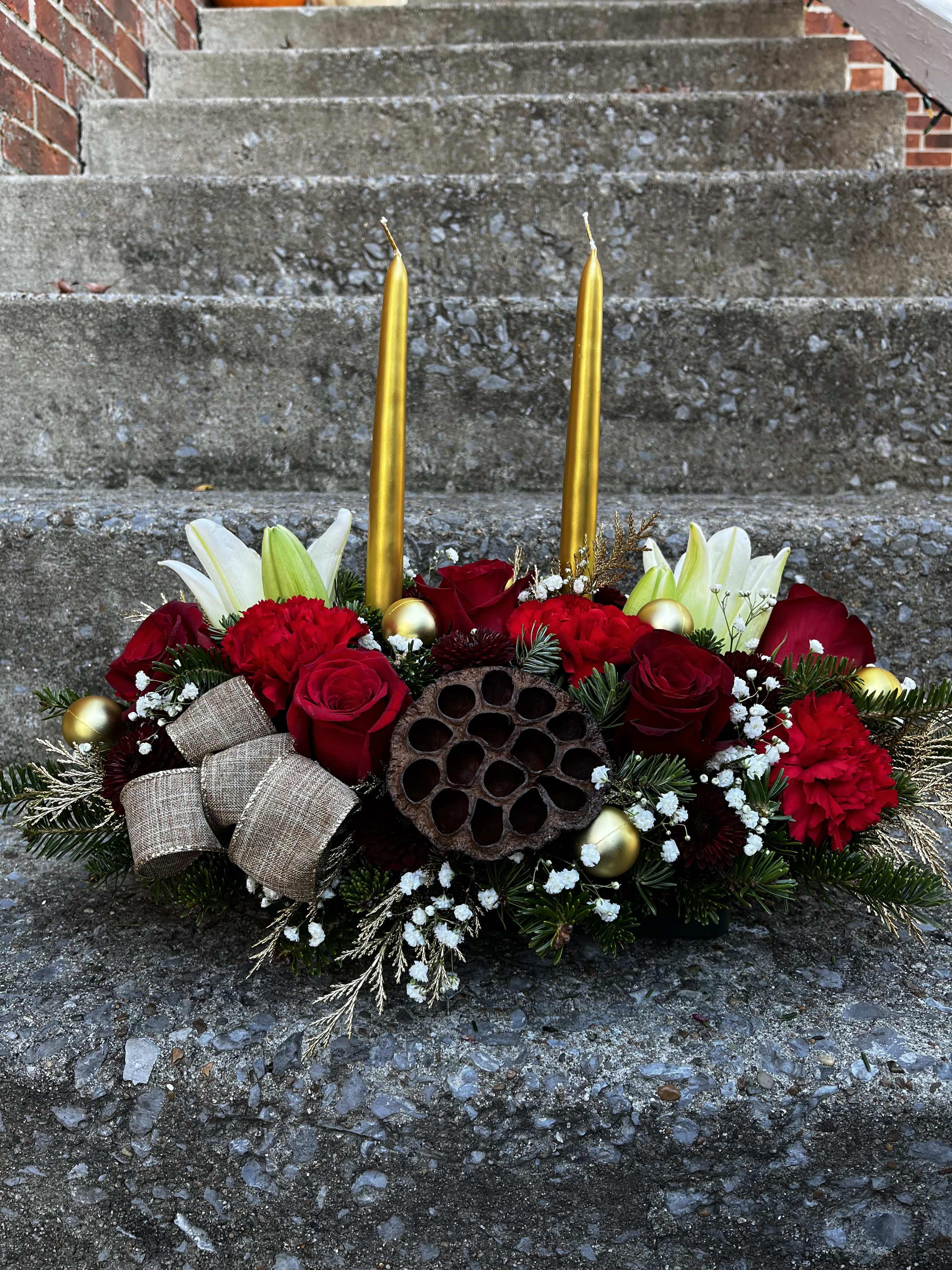 Jingle Bell Rock - This centerpiece has roses, lilies, carnations, mums, a pinecones, ribbon Tuffs, Christmas ornaments, babies breath, Christmas greens, golden colored Christmas greens, pod, and two pomegranate colored candles.