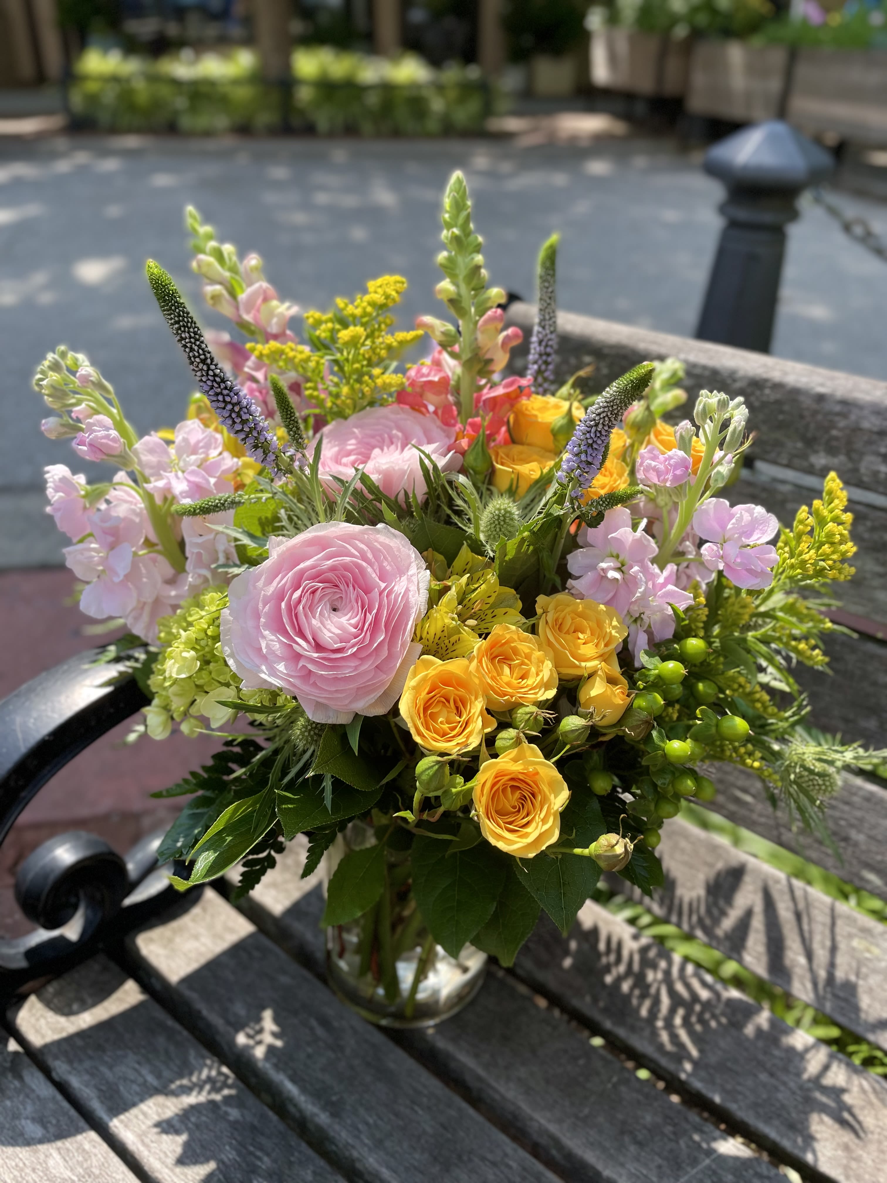 Solara - Bursting with the joyful hues of a sunny day, Solara Serenade is a radiant floral arrangement that sings of warmth, laughter, and carefree moments. Soft blush ranunculus, and lavender veronica add a romantic note, white golden spray roses and vibrant yellow solidago infuse energy and brightness.  Perfect for brightening a loved one's day or celebrating life's simple pleasures, this garden-inspired bouquet brings nature's harmony right to your heart.