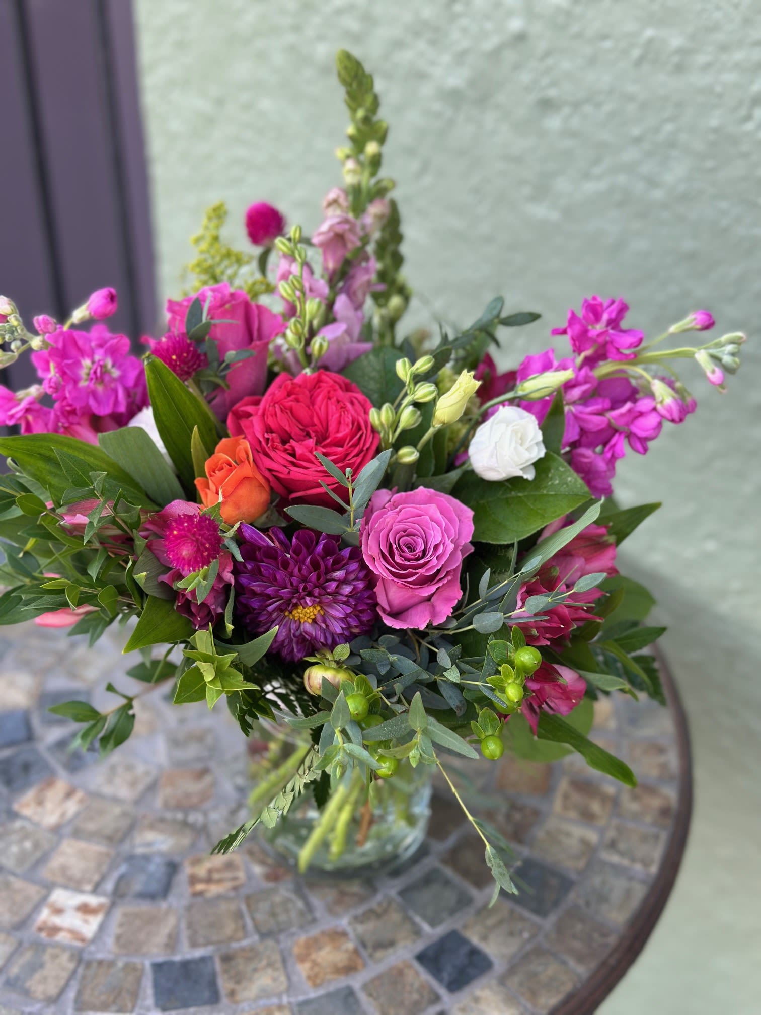 Taylor &amp; Travis - In honor and excitement of the Swift-Kelce engagement this arrangement is bursting with rich jewel tones and lush textures. Taylor &amp; Travis is a celebration of bold beauty and love. Featuring radiant roses, playful pops of orange, vibrant stock, and striking dahlias, it’s accented with fresh greenery for a natural finish. Nevertheless, this is perfect for birthdays, celebrations, or simply brightening someone’s day, this bouquet is designed to make a statement of joy and love.