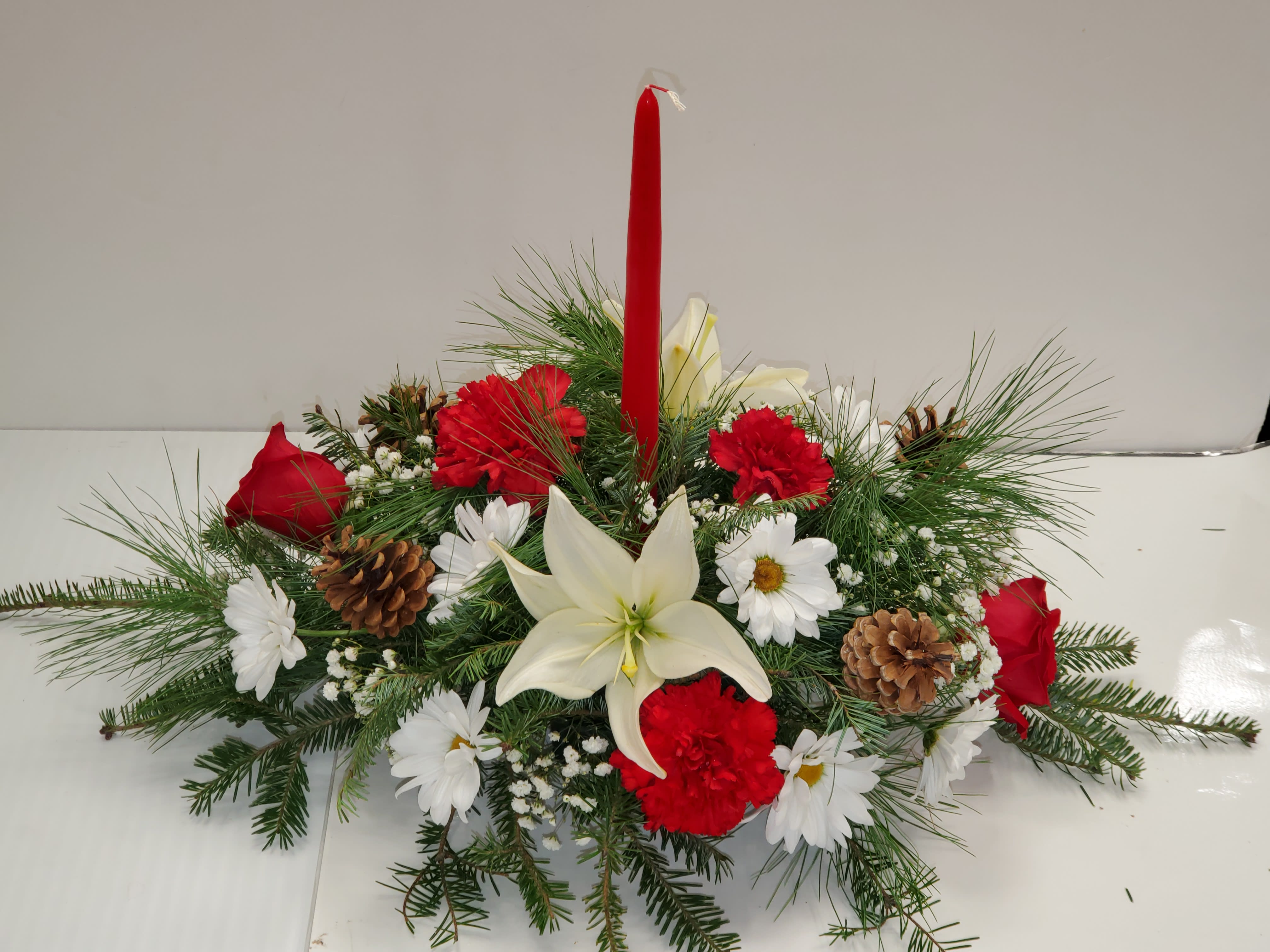 Classic Christmas centerpiece - Standard: Christmas green,  1 red candle 2 red roses, 4 red carnations, 2 white lilies, 3 white daisies or cushions, 4 pine cones, BB.  Deluxe : Christmas green, 4 red roses, 4 red carnations, 2 white lilies, 3 white daisies or cushions, 4 pine cones, BB, r 3 red mini carnations, 2 red candles, 6 Christmas ornaments.  Premium: Christmas green, 6 red roses, 4 red carnations, 4 white lilies, 3 white daisies or cushions, 4 pine cones, BB, 3 red mini carnations, 2 red candles, 6 Christmas ornaments.