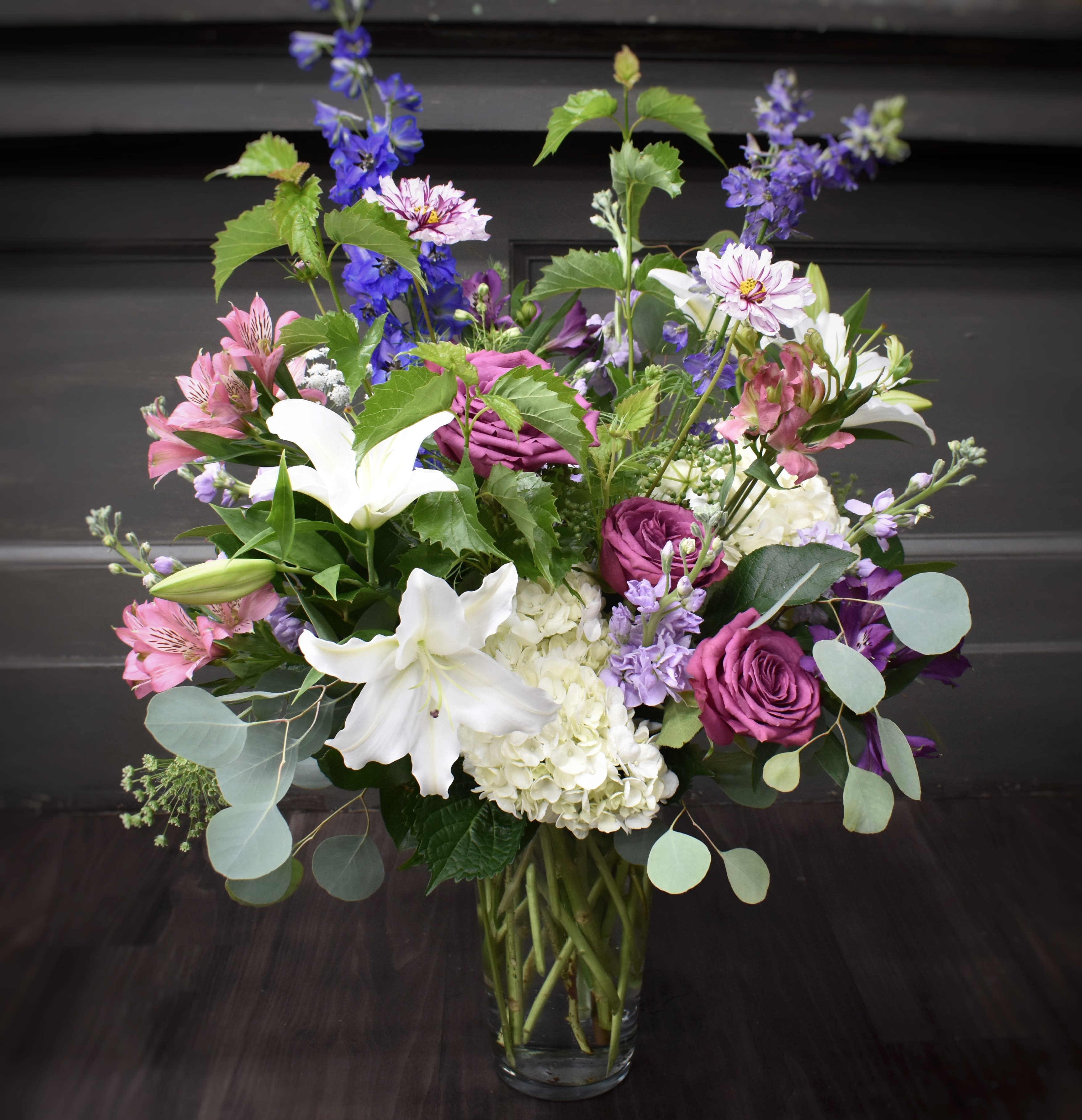 Garden Delight - A bouquet showcasing the elegant pairing of lavender and white blooms evokes a sense of serenity, purity, and grace. This larger vase of flowers includes, lilies, roses, alstroemeria, Larkspur, hydrangea and other garden like accent flowers. 