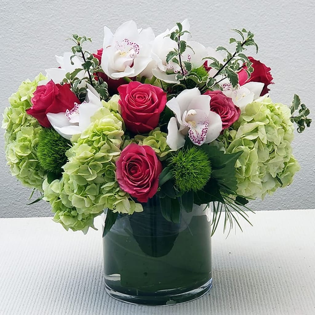OC Blossom Arrangement - OC Blossom flower arrangement of hot pink roses offset with green hydrangea and then topped with fresh-cut cymbidium orchids and seasonal accents. Bouquet delivery comes in a glass cylinder vase ready to be enjoyed. Approximately 18&quot; H x 18&quot; W. 