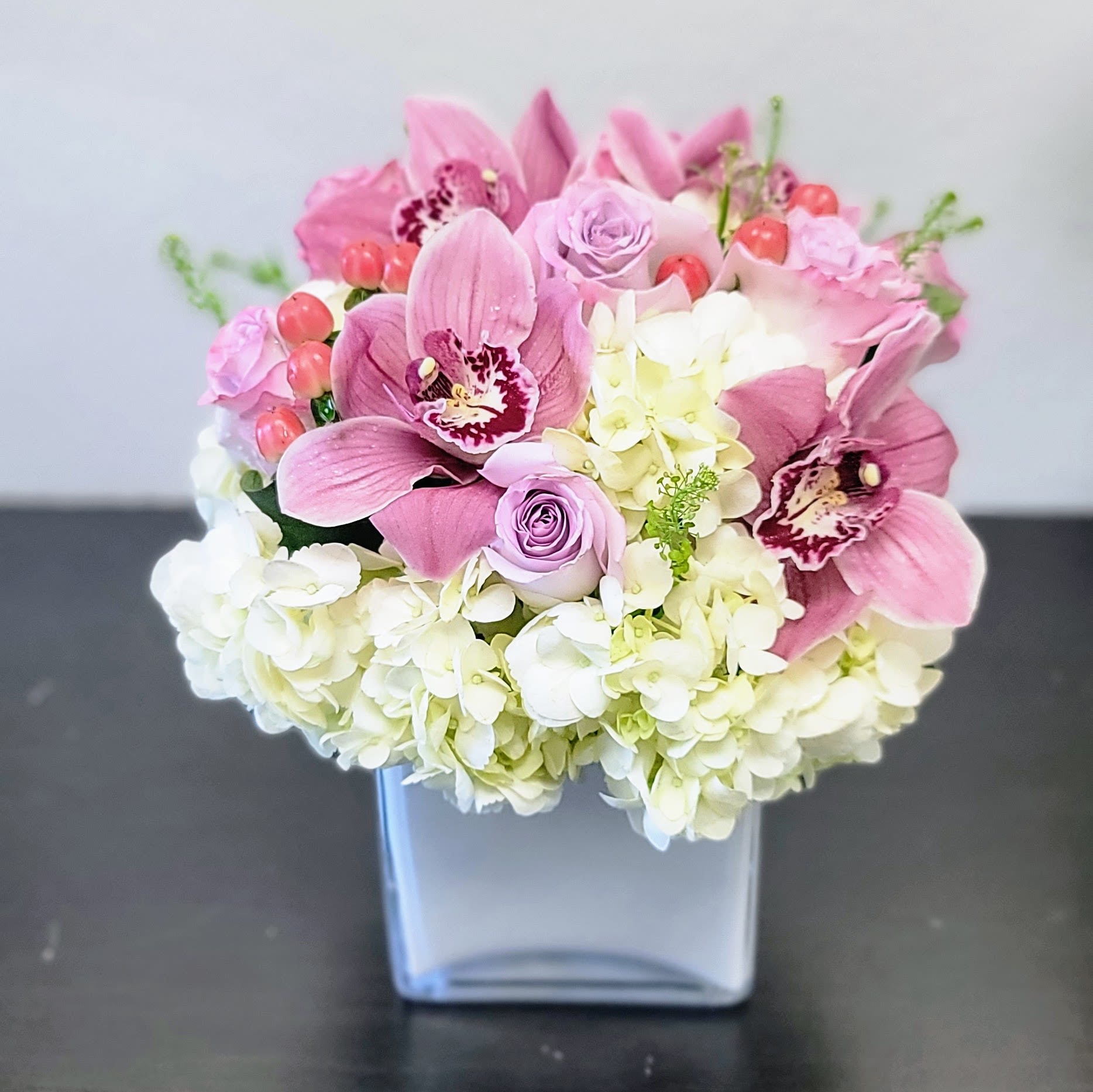 Pop of Lavender - Featuring vibrant pink Cymbidium Orchids, soft lavender Roses, and white Hydrangeas, this arrangement exudes refined beauty. Accented with charming red berries.  Perfect for birthdays, anniversaries, Mother's Day, or just because.  Approximately 12&quot; H x 10&quot; W. Order now for a touch of luxury!