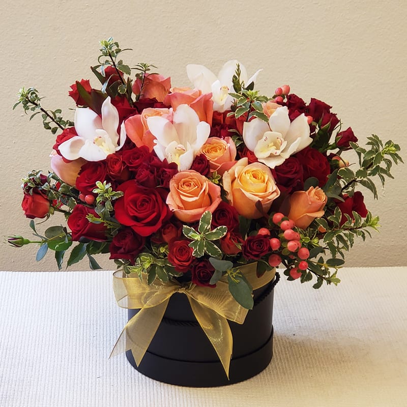 Set to Celebrate Hat Box Arrangement - Capture the beauty of the moment with our Charm Celebrate Hat Box Arrangement. Our flower experts finish this arrangement in a round black box with a combo of red roses, spray roses, garden roses, ranunculus, orchids, and seasonal accents. Whether you're saying thank you to a special friend or celebrating a most exciting occasion, this breathtaking arrangement is undoubtedly a lovely and luxurious gift for your loved ones to cherish.  Approximately 16&quot; H x 14&quot; W.  