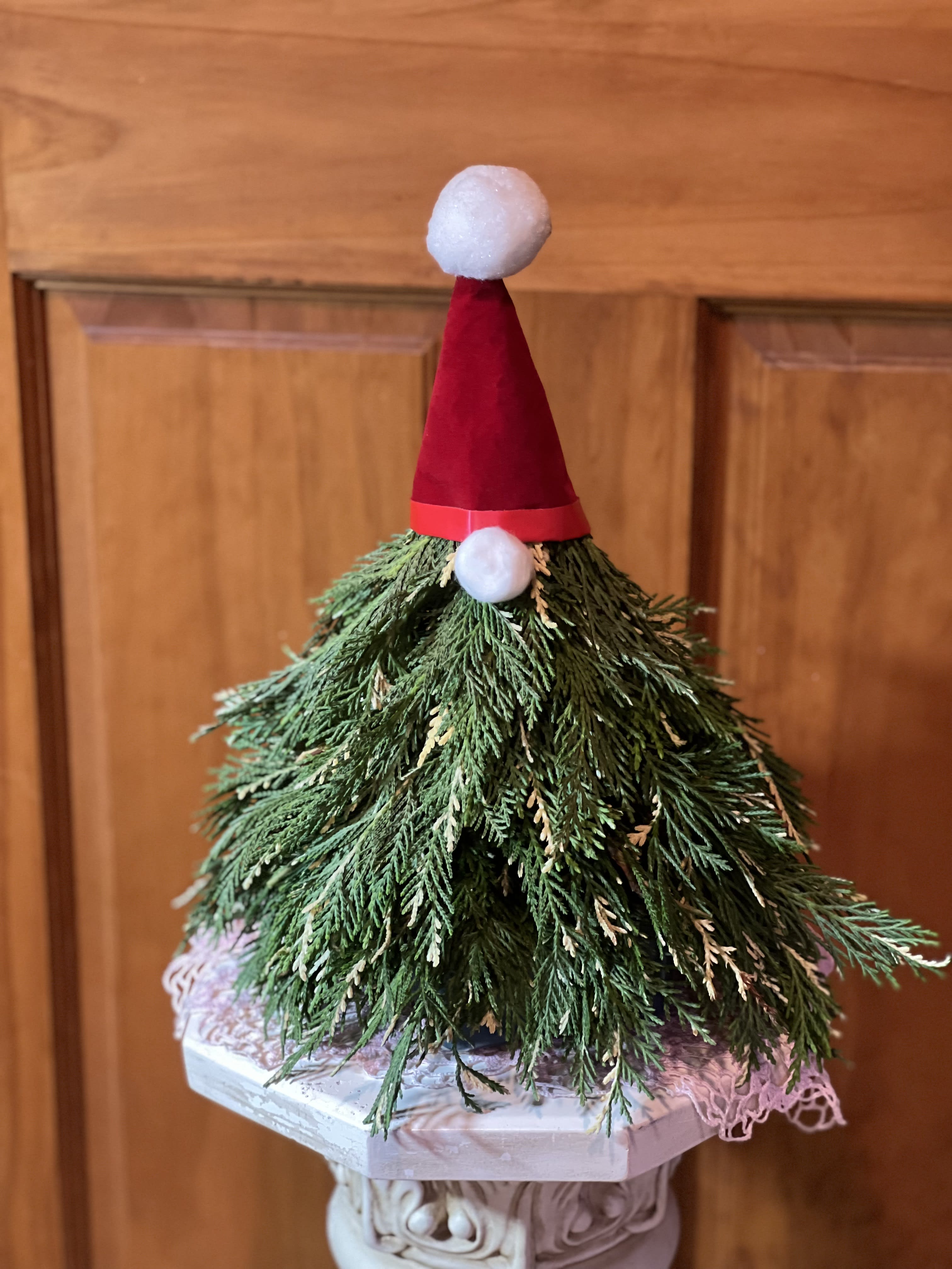 Christmas Tree Gnome - Our Christmas Tree Gnome is a seasonal item. Great to brighten your doorway or entryway. Custom created with variegated cedar on a Medium tree foam placed into a waterproof container to hold water. Topped with a red velvet ribbon hat and topped with a snowball fluff ball. The nose is a small cotton like orb. Allow us extra time to create this one. Overall size is over 12&quot; tall. Our Deluxe Christmas Tree Gnome is on a Large tall tree form. Overall size is over 14&quot; tall. Premium will be on the Large tree form, but with the addition of fresh flowers attached to the body of the Gnome. Overall size is over 14&quot; tall.