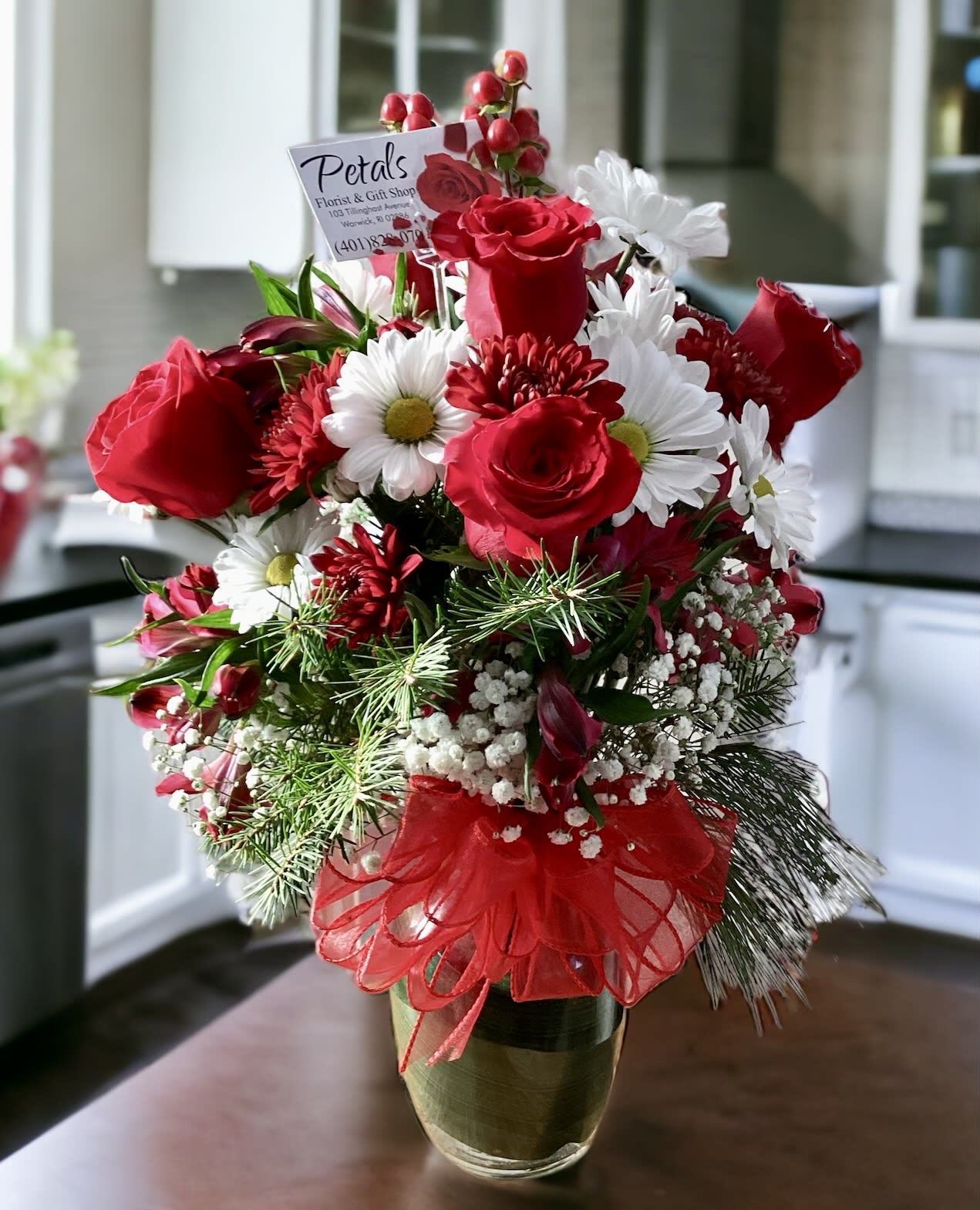 The Cheerful Giver… by Petals - Be The Cheerful Giver this Christmas with this Enchanting Winter Design by Petals. Perfect for any occasion this winter season. I am featuring red roses, White Daisies, burgundy daisy poms, red hypericum berries, pine cones, and a variety of sweetly scented winter greens, bows, and message cards. Please feel free to call me at 401-828-0701 if you have questions. On occasion, flowers may vary slightly due to daily availability. Thank you, Cheryl