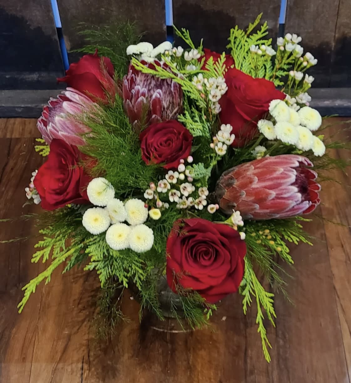 Christmas in San Francisco - This design is a 360 centerpiece with classic holiday colors. Protea, roses and mums are accented by a variety of winter foliage.