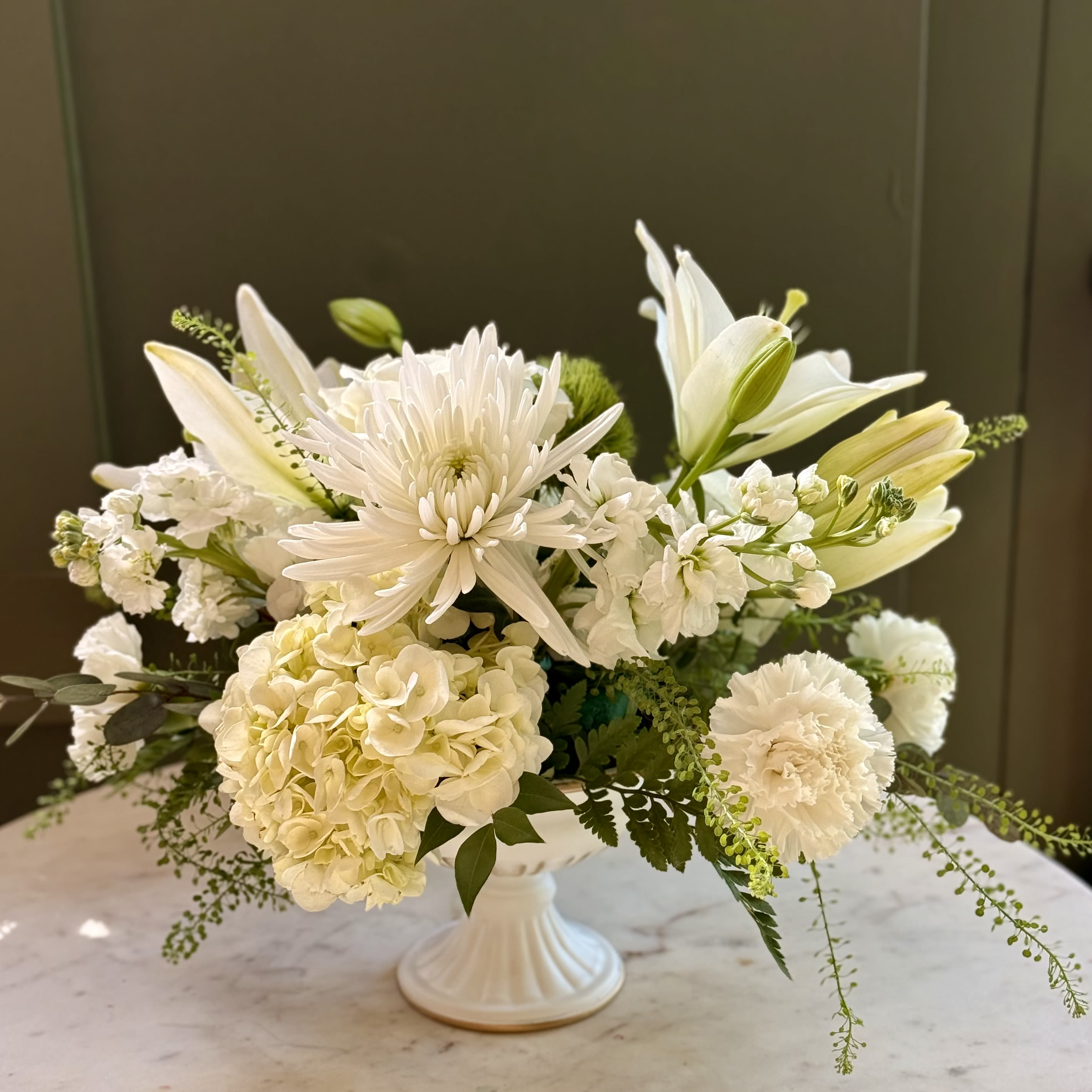 Snowfall - An all white and green winter floral design for moments that deserve a touch of elegance this holiday season. Featuring: - White Hydrangeas - White Cremone - Asiatic White Lilies - White Stock - Green Trick - Styled with premium seasonal foliage Presentation Options: White urn (5&quot; H, included in price) Every order includes: A custom message card - simply enter your message at checkout and we'll take care of the rest. Please note: Flowers are subject to seasonal availability. If a listed flower is unavailable, our designers will substitute it with flowers of a similar shape, color, and style to maintain the overall aesthetic.