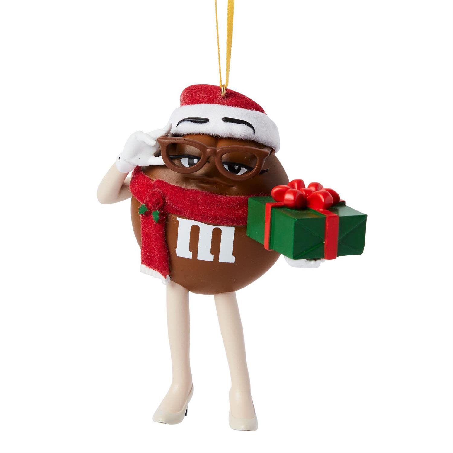 M&amp;M’S Ms. Brown Holiday Ornament - Bring a touch of iconic holiday charm to your tree with the M&amp;M’S Ms. Brown Holiday Ornament. Recognizable from the beloved seasonal commercials enjoyed around the world, Ms. Brown brings her signature wit, style, and understated confidence to the festivities. Dressed in a Santa hat and cozy scarf, she offers a neatly wrapped present—because the holiday season is always sweeter with a little M&amp;M’S magic.  Standing 3.75 inches tall, this hanging ornament adds a playful and nostalgic touch to any Christmas display. Whether you’re a longtime fan of the characters or simply love a fun pop of personality on your tree, Ms. Brown is ready to ring in the season with delicious holiday spirit.  Each ornament is sold individually and available in limited quantities—a perfect treat for collectors and candy lovers alike.