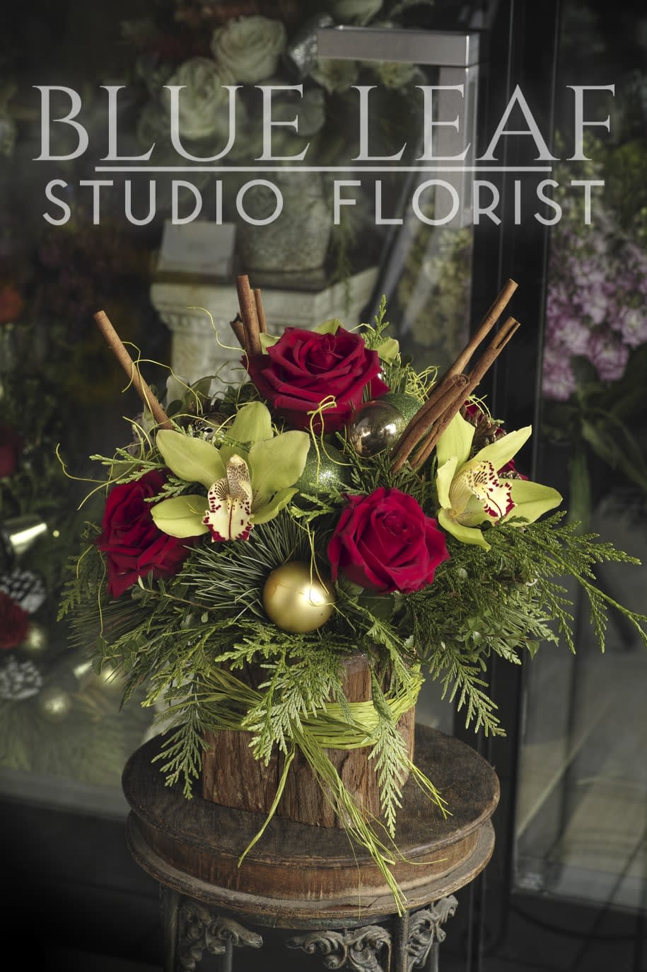 Christmas Cymbidium Orchids - A fragrant holiday centerpiece with red roses, cymbidium orchids, cinnamon sticks and shining ornaments in a wooden vase.