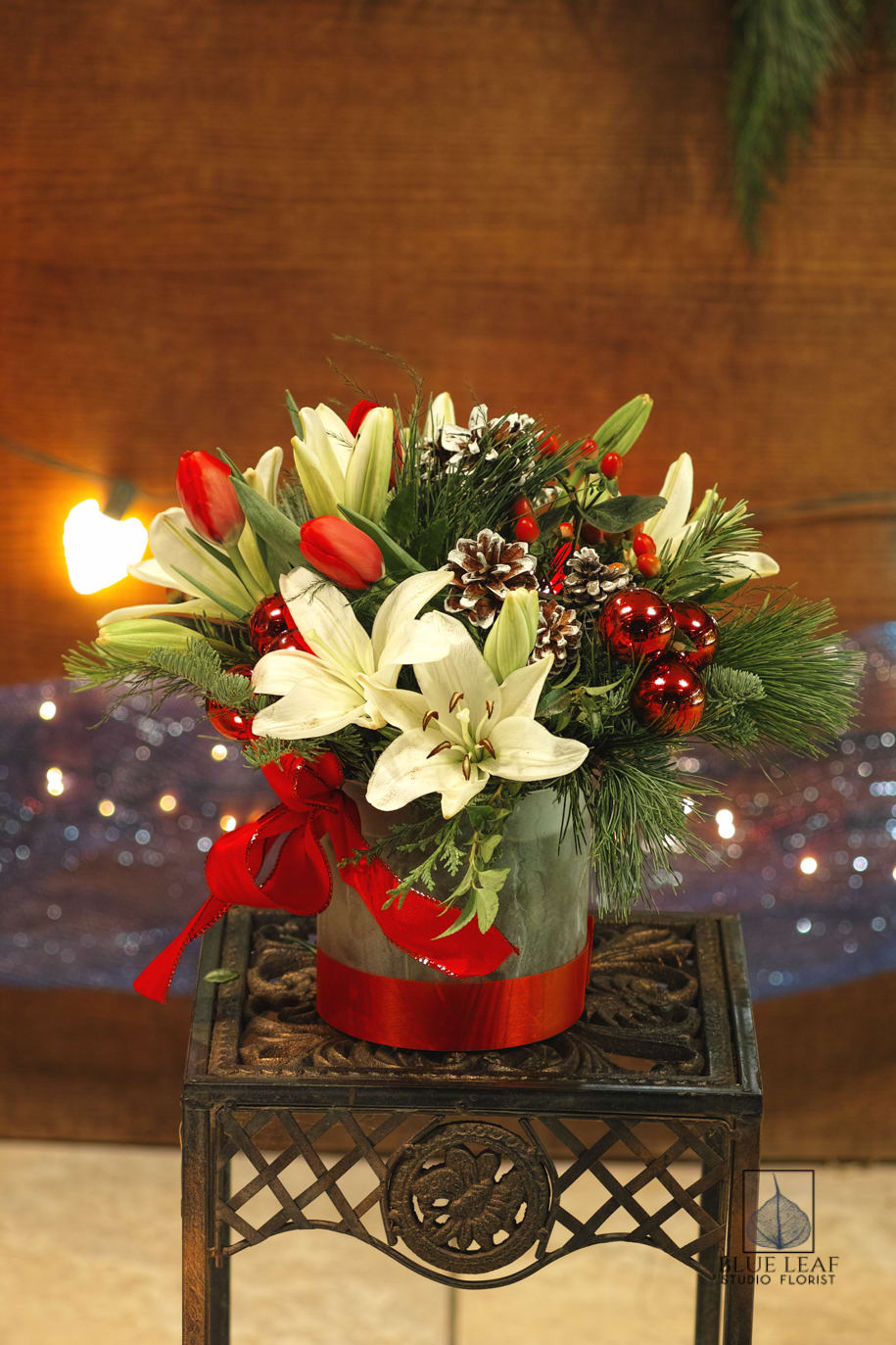 Christmas Surprise - A perfect holiday centerpiece designed with white lilies, tulips, shining red ornaments and pinecones.