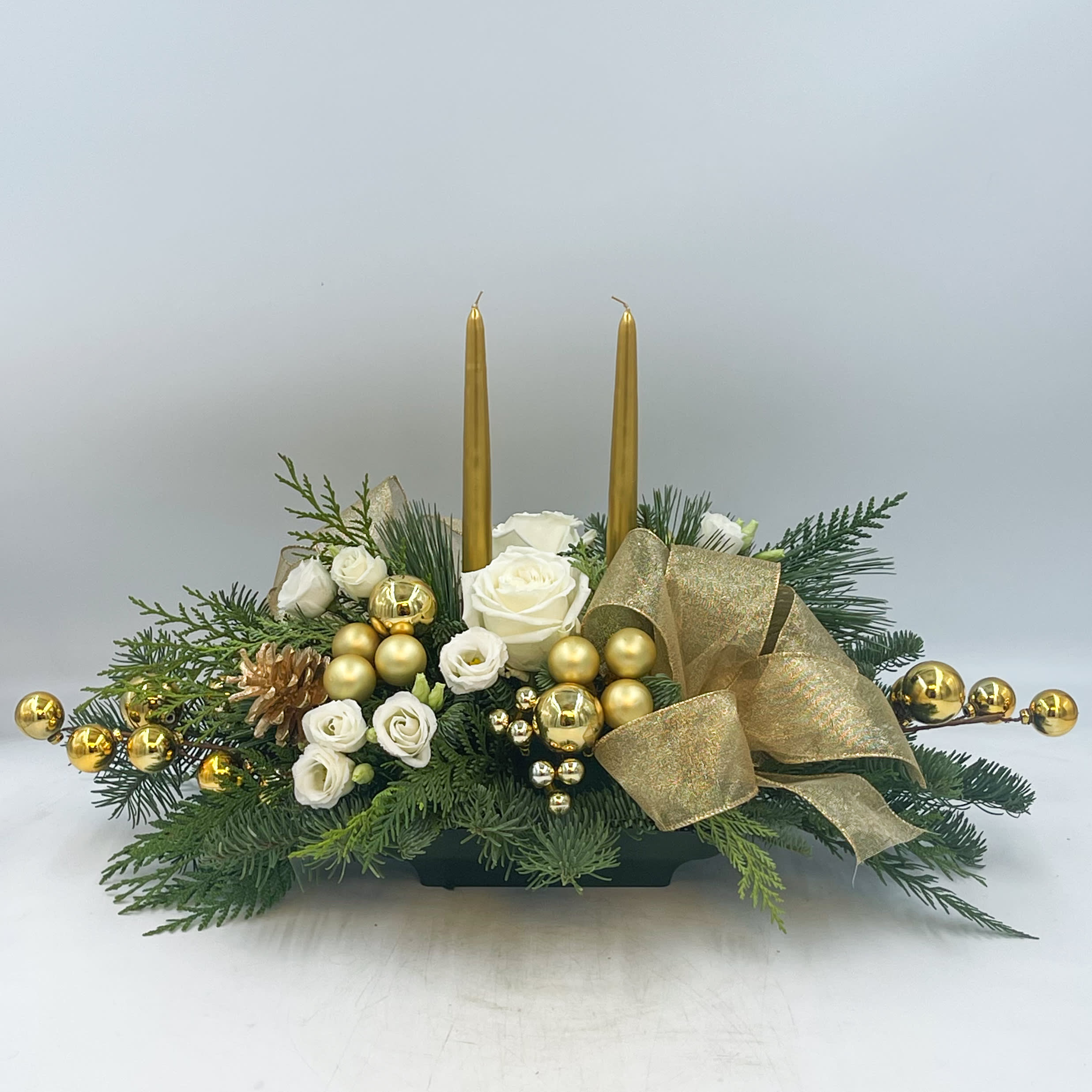 Christmas Dreaming - A beautiful gold and white Christmas Centerpiece, Christmas Dreaming features Gold Candles, Gold Pinecones, Gold Ornaments and Ribbon, White Lisianthus and White Roses in a bed of mixed evergreens.