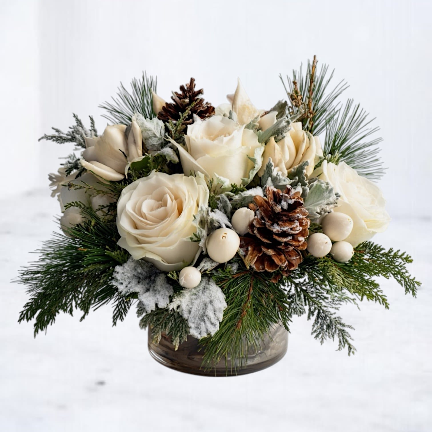 Snowfall Grove - Inspired by the stillness of a snowy winter morning, the Snowfall Grove Arrangement features ivory roses surrounded by frosted evergreens, lamb’s ear, white berries, and natural pinecones. Designed in a lined glass vase, this arrangement blends texture and softness for a cozy, elegant winter aesthetic.  Each piece is handcrafted by Whiskey Wallflower using premium seasonal greens and snow-kissed accents, making it a beautiful choice for holiday tables, winter gifting, or adding a serene touch to your home décor. Its neutral palette pairs effortlessly with any interior style, from rustic to modern.