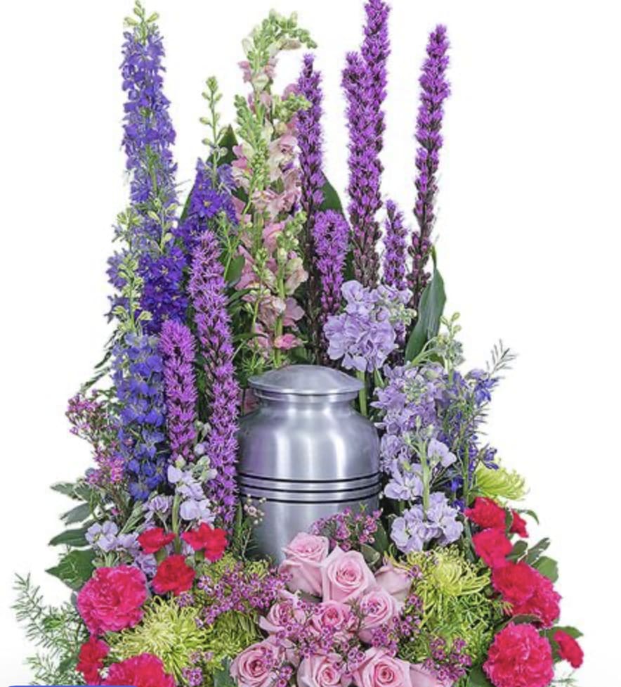 Eternal Peace Urn Surround pre order - Soft, soothing, and beautifully symbolic, the Eternal Peace Surrounded offers a serene tribute to a life cherished and remembered. Tall spired of lavender, purple, and soft pink blooms rise gently behind the urn, creating a natural, peaceful backdrop that evokes the feeling of quit garden at dawn.  Surrounding the base are delicate roses, carnations, and seasonal flowers in blush, mauve, and soft pinks- each chosen to reflect love, grace, and the comfort of lasting memories. Lush greenery adds fullness and depth, completing the design with tranquility and elegance. This arrangement is thoughtfully crafted to frame the urn with beauty and reverence, offering solace and honoring the journey of a loved one with tenderness and respect.