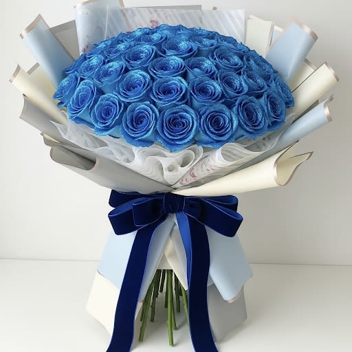  Sapphire - Sparkling Jewel Roses By Black Cat Florist  - A spectacular and modern "Sapphire” buchón style bouquet featuring 50 long-stemmed roses in a brilliant, shimmering blue. Each rose is covered in a layer of fine blue glitter, giving the entire bouquet a truly magical sparkle. It is beautifully wrapped in a combination of soft-toned Korean papers in shades of blue and white, and finished with a velvet ribbon bow in a rich navy blue.  Short stems starts at $225.