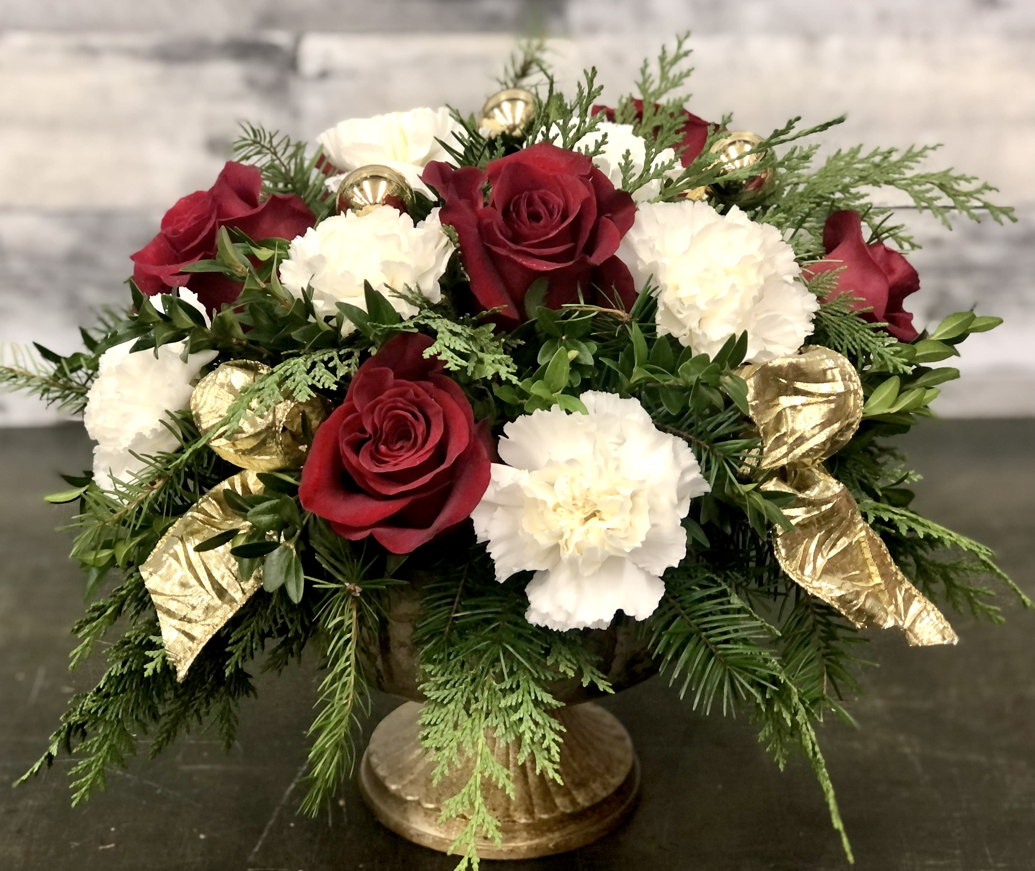 Holiday Cheer - Roses and carnations with winter greens and ribbon tails fill a holiday  container.  Perfect for your holiday table!