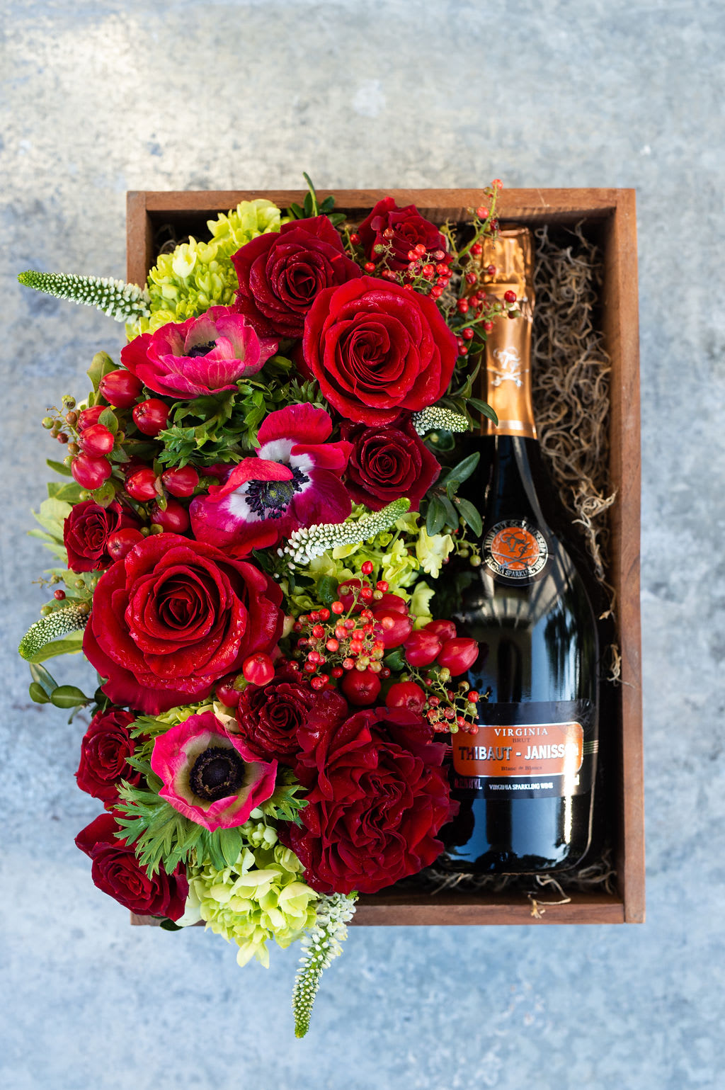 Blanc De Chardonnay Holiday Day Gift Box - Our best-selling wine box is now available in a festive variation -- just in time for the holidays!  A beautiful wooden gift box, locally hand-crafted from reclaimed wood. A 750ml Thibaut-Janisson Blanc De Chardonnay rests on a bed of Spanish moss, alongside a beautiful bed of flowers in the pavé style. *Wine and cider selections curated with care by Market Street Wine Shop.*  Wine Description: This is a truly historic offering, putting Virginia in conversation with the great wines of France’s champagne region. Made from 100% chardonnay grapes, this wine manages to be rich and dry at the same time. This is a bottle made for every kind of celebration. Bubbles go with everything!  Before placing your order, please ensure that the recipient is above 21 years of age and will be home to receive the delivery, as ABC regulation requires that we check photo ID upon delivery.  If no one is present at the delivery site, delivery cannot be completed.