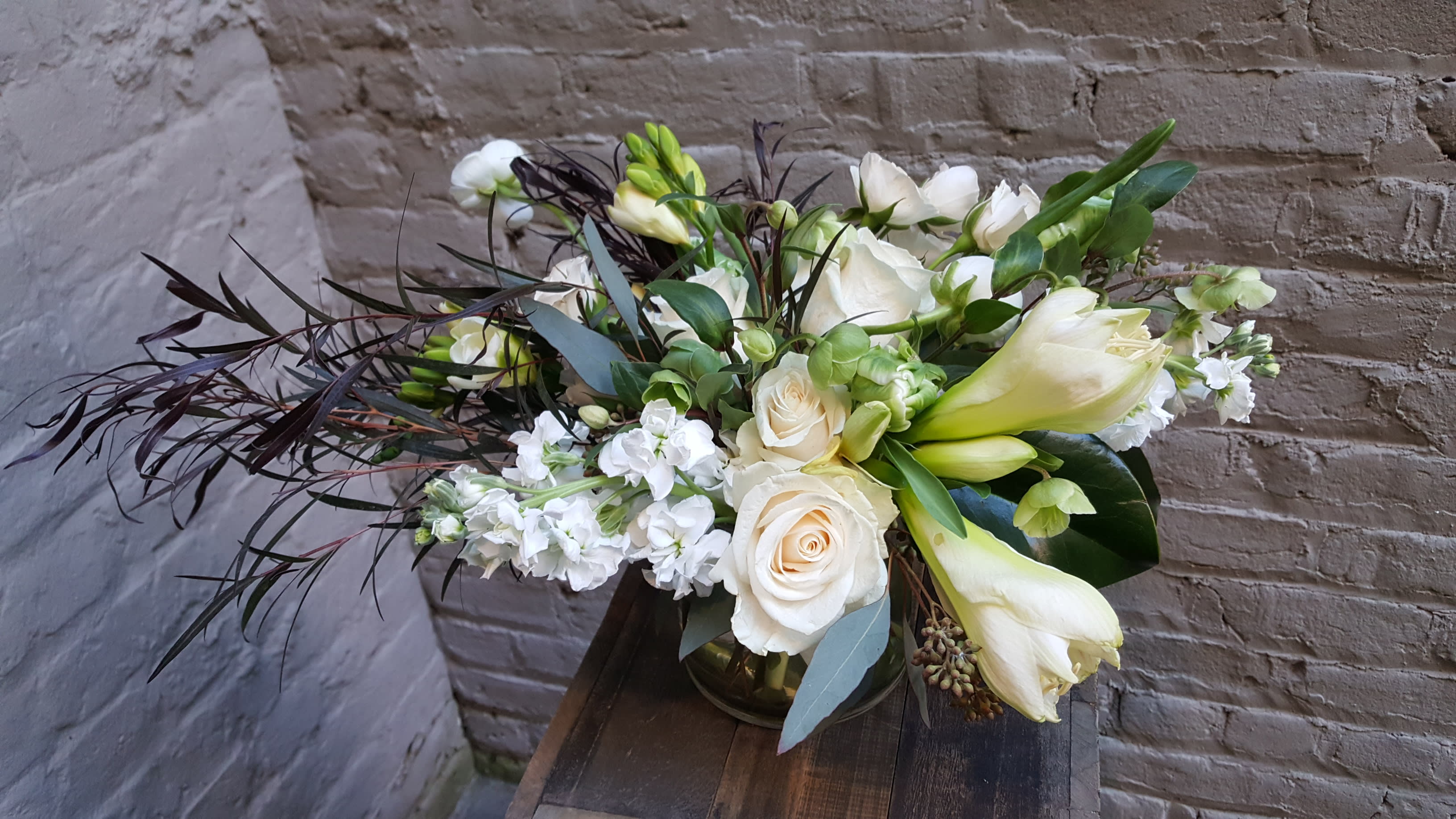 The Snow Queen - A clear glass vase filled with an enchanting array of crisp snow white flowers and a dash of spring green peeking through -- including amaryllis, parrot tulips and hellebores -- and accented with wonderfully contrasting dark plumes of agonis foliage.