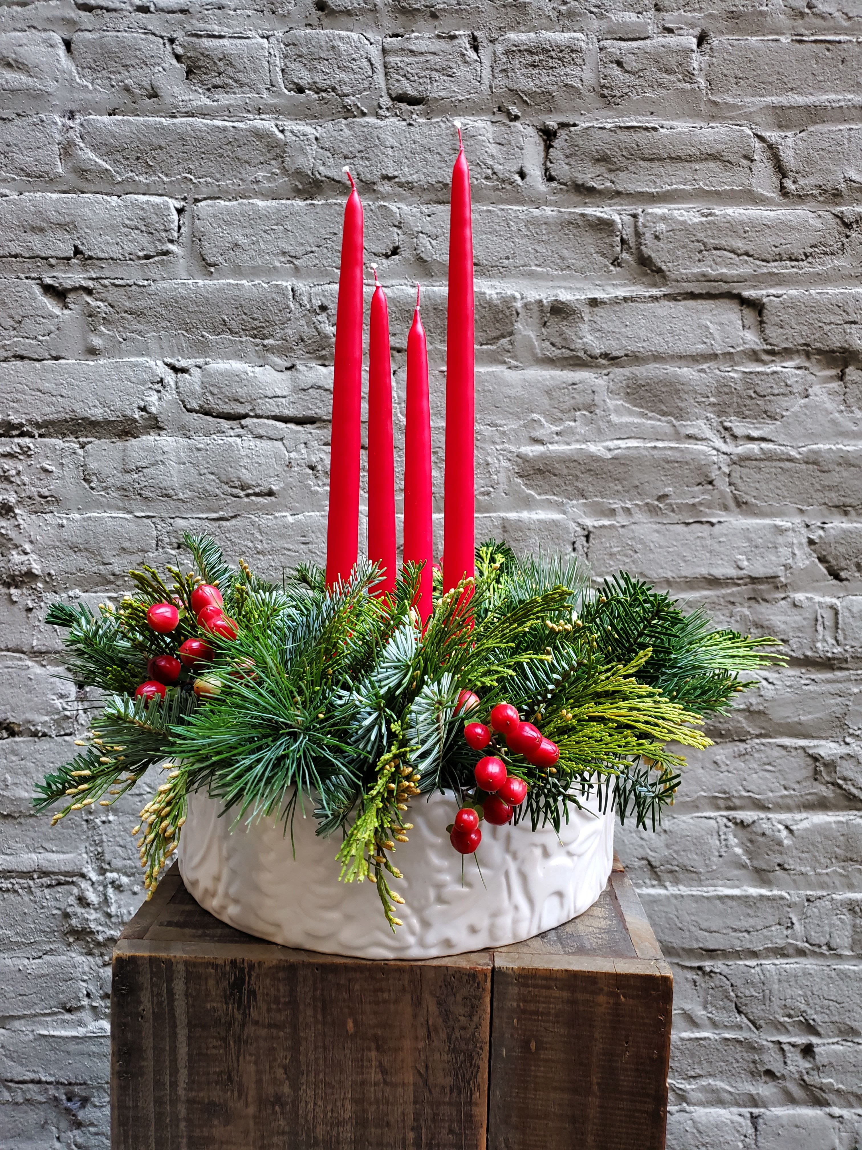 Christmas by Candlelight - A perfect arrangement to gather 'round with your closest friends and family!  This unique white ceramic vessel (featuring a bas-relief forest scene) is filled with fresh berries and fragrant fir, cedar and pine.  Four red taper candles arise from the center, creating a truly warm and inviting display.  Arrangement vessel measures 11.5&quot; wide.