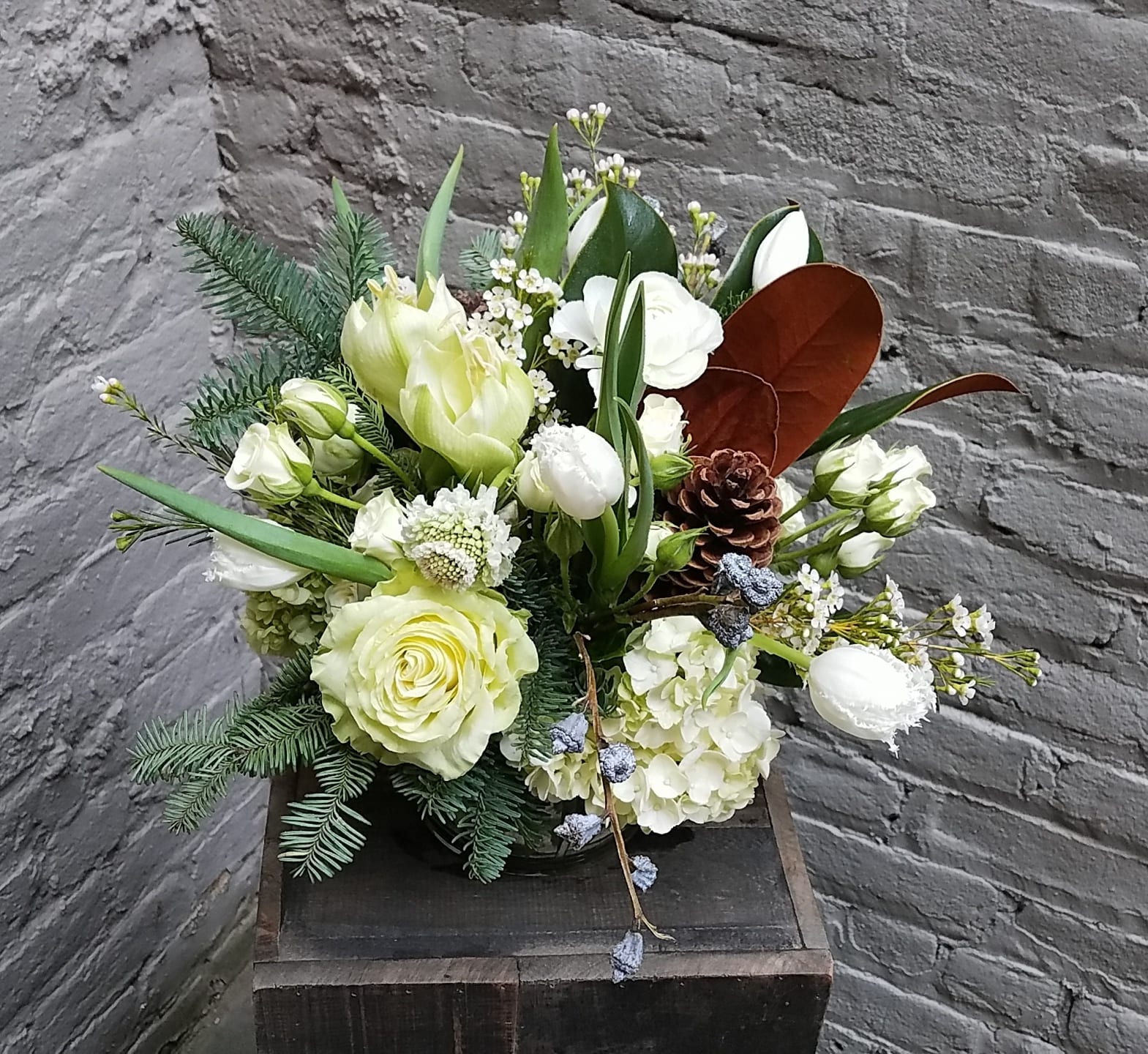 Into The Woods - A clear glass vase filled to the brim with a collection of blooms in shades of whites and greens; including roses, amaryllis, green hydrangea, and white tulips -- as well as woodsy accents of pinecones and evergreens.  Arrangement measures approximately 13x13&quot;.