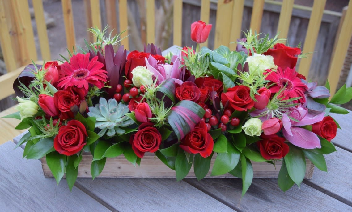 Holiday Flower Box Centerpiece - Flower box centerpiece is created with premium flowers arranged in a wooden planter 18x5x3 in a classic red and green color scheme. Selection of flowers depends on availability but the floral designer carefully picks the freshest mix of flowers to create a stunning low centerpiece to celebrate Christmas.