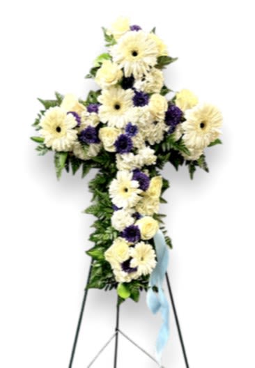 Blue Serenity Memorial Easel - The &quot;Blue Serenity Memorial Easel&quot; is a beautifully crafted tribute designed in the shape of a cross, symbolizing faith and hope. Adorned with a delicate arrangement of white gerbera daisies, soothing blue ocean mums, soft white roses, and elegant white hydrangeas, it creates a peaceful and comforting display. These flowers rest on a lush bed of mixed greens, adding depth and vibrancy to the arrangement. A gentle baby blue bow accents the easel, enhancing its serene and calming presence. This memorial easel serves as a heartfelt tribute, offering a sense of tranquility and remembrance for loved ones.