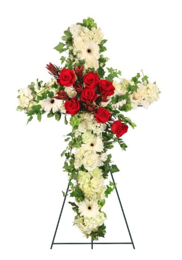 Peaceful  Crossover in Red Easel - This striking sympathy tribute, elegantly displayed on a 54-inch easel, features a beautifully crafted 24-inch wet floral foam cross that serves as a poignant symbol of faith and remembrance. Adorned with lush foliage of variegated ivy and pittosporum, the arrangement exudes a sense of serenity and peace. Three pale green hydrangeas provide a touch of softness and compassion, while six pristine white gerberas and ten classic white roses embody purity and love, creating a calming effect. Three bells of Ireland add a unique touch of hope, complemented by the vibrant energy of six green carnations that signify a celebration of life. In stunning contrast, six rich red roses bring a deep sense of love and remembrance, while three safari sunset leucadendrons introduce a hint of warmth and resilience. Together, this heartfelt arrangement honors the life and legacy of a beloved individual, offering comfort and solace to all who gather in their memory.