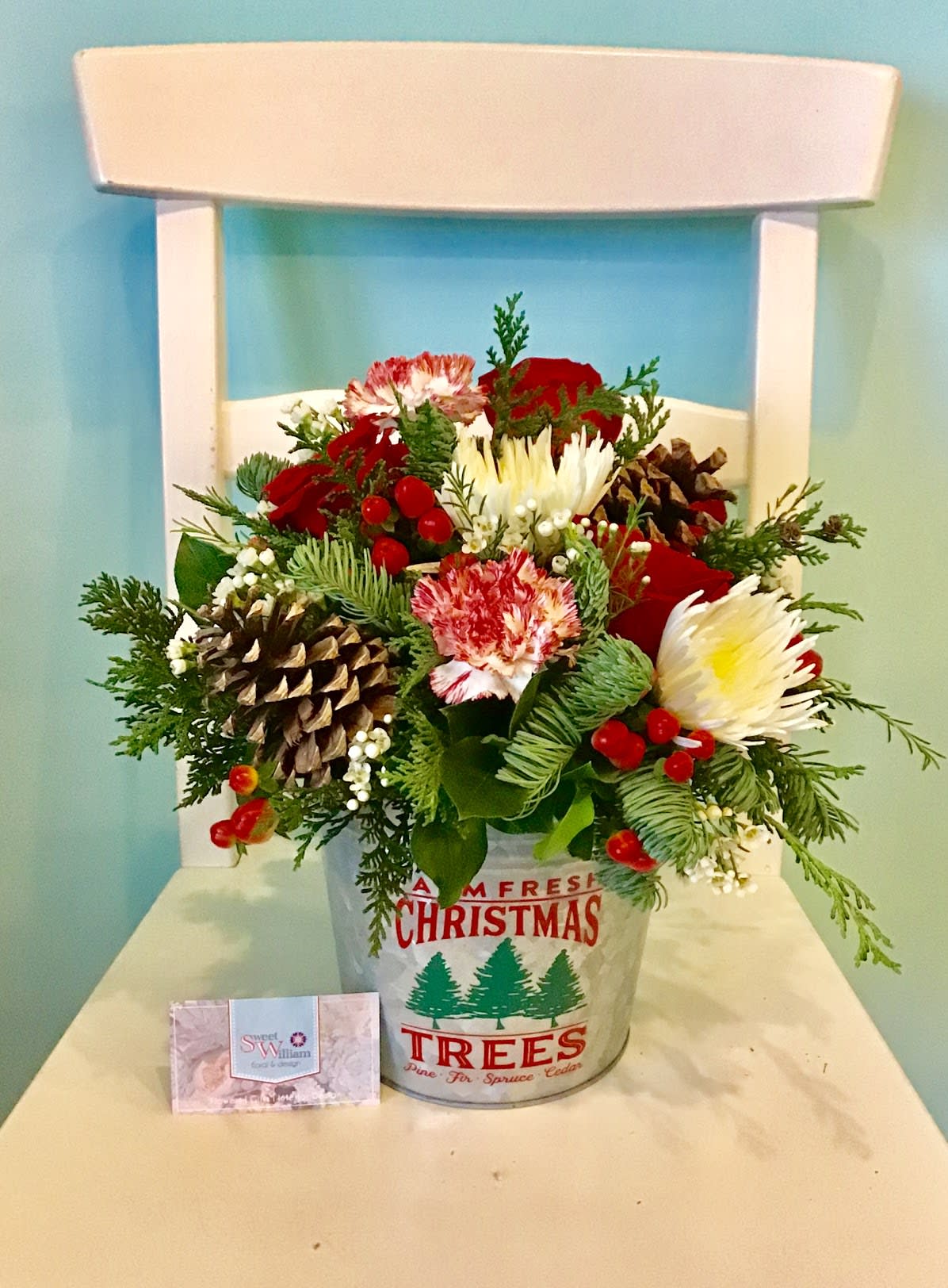 Farm Fresh Christmas - Looks great on kitchen tables or office desks! Send a little Christmas country charm in a tin container! This arrangement comes with roses, chrysanthemums, carnations, wax flower, hypericum berries, and pinecones. 