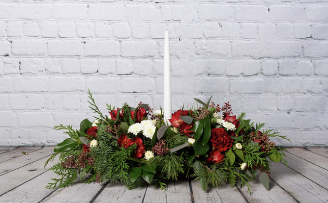 Single Candle Holiday Centerpiece  - Dress your holiday table up this season with this traditional centerpiece  favorite! Carnations, chrysanthemums, hypericum berries, and pinecones come together with fresh seasonal greens to make this arrangement a beautiful addition to your holiday celebration!