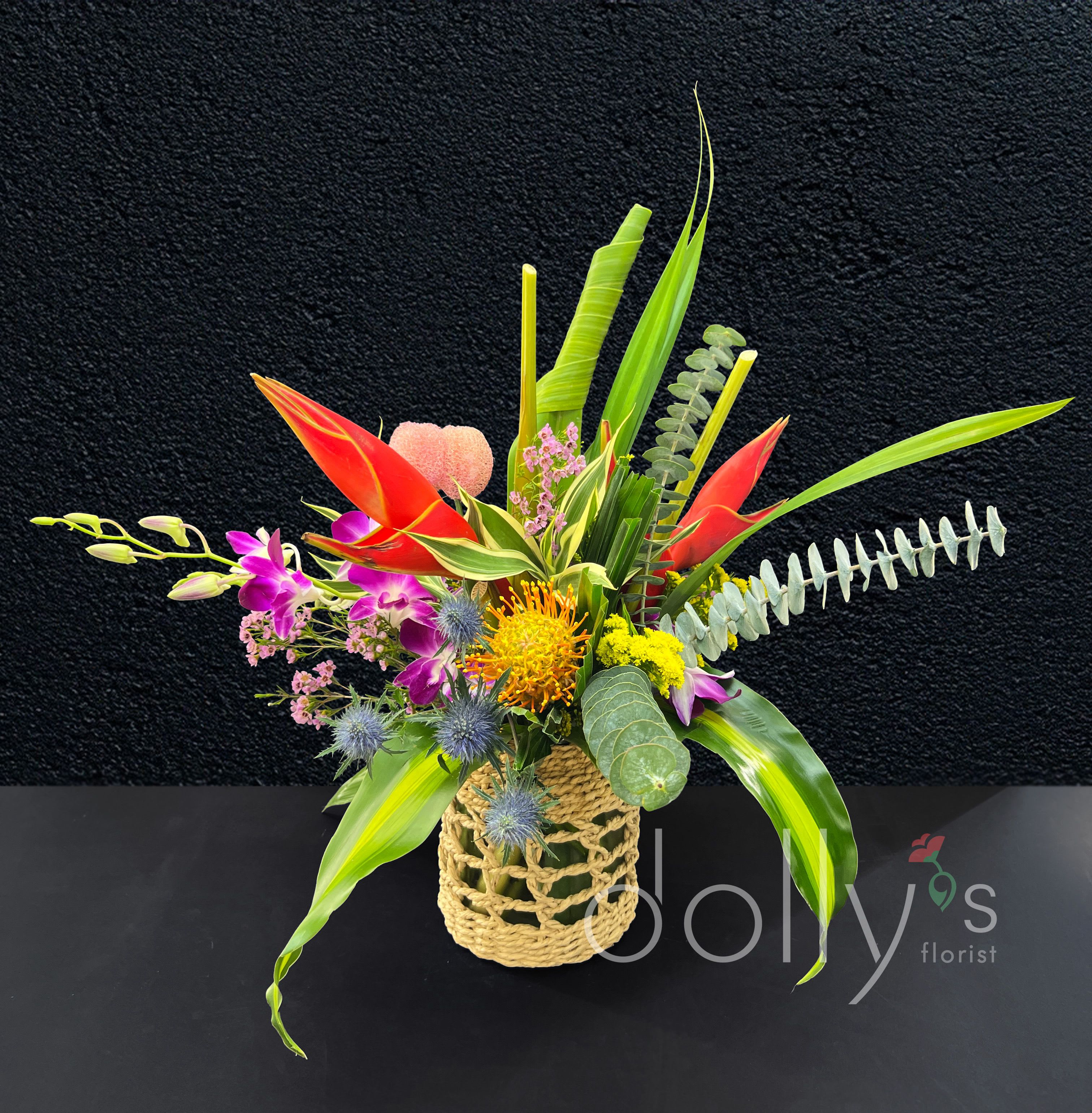 Tropic Like It's Hot - Celebrating love and humidity ;). Composed of tropical blooms within a glass vase surrounded by a braided rope.