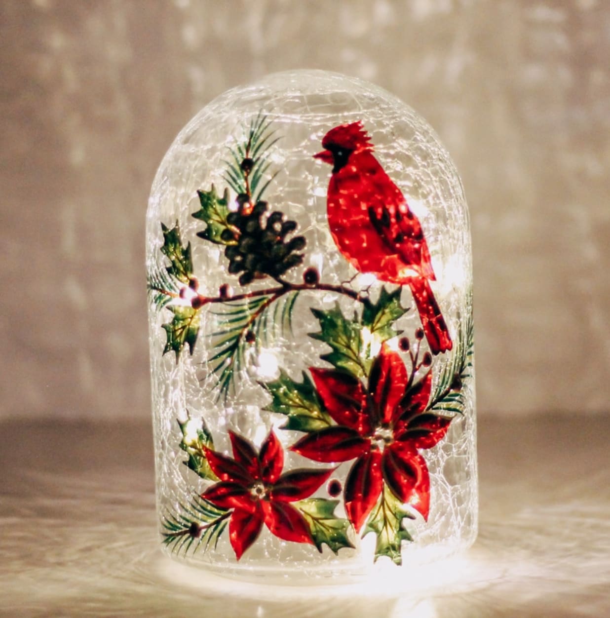 Cardinal Glow Crackle Glass Dome - This beautiful crackle-glass dome features a vibrant red cardinal perched among pine, poinsettias, and holly. Soft LED lights illuminate the painted design from within, creating a warm and festive glow. Perfect for tabletops, shelves, or holiday centerpieces, it adds a charming touch of Christmas elegance to any space. 5&quot; W x 8&quot; H