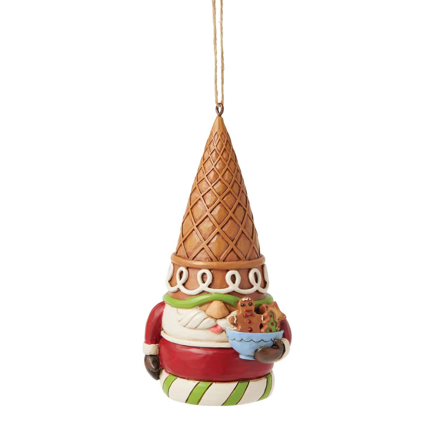 Gingerbread Gnome Ornament - Add a sprinkle of whimsy to your holiday décor with this delightful Gingerbread Gnome Ornament from the Jim Shore Collection. Crafted in the style of a festive gingerbread cookie, this charming gnome is decorated with red and green icing, playful sprinkles, and a cheerful peppermint-striped base. Topped with an oversized ice cream cone hat and holding a bowl filled with candy and gingerbread treats, he brings an irresistibly sweet spirit wherever he goes.  Standing 4.375 inches tall, this hanging ornament is beautifully hand-painted and sculpted with Jim Shore’s signature folk-art detailing, from carved textures to decorative flourishes that evoke nostalgia and holiday magic. Every detail makes him a joyful, eye-catching addition to your Christmas tree.  Each ornament is sold individually and available in limited quantities, making it a sugary-sweet collectible for fans of Jim Shore, lovers of gingerbread décor, and anyone who enjoys a touch of whimsy during the holidays.