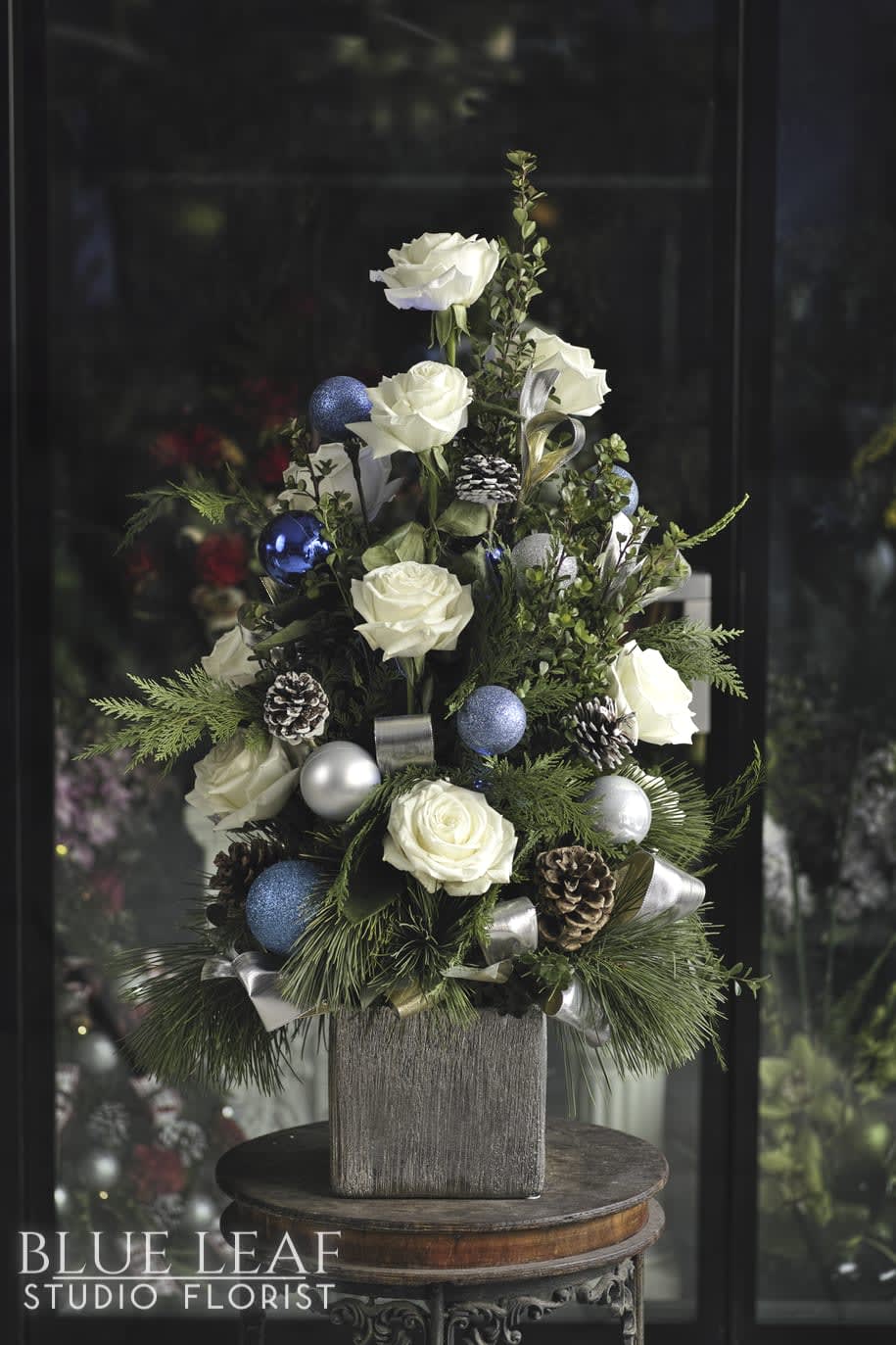 Winter Wonderland  - An eye catching winter arrangement in the shape of a Christmas tree. Elegant white roses and pinecones are styled in a beautiful silver vase, and accented with ornaments and battery operated lights.