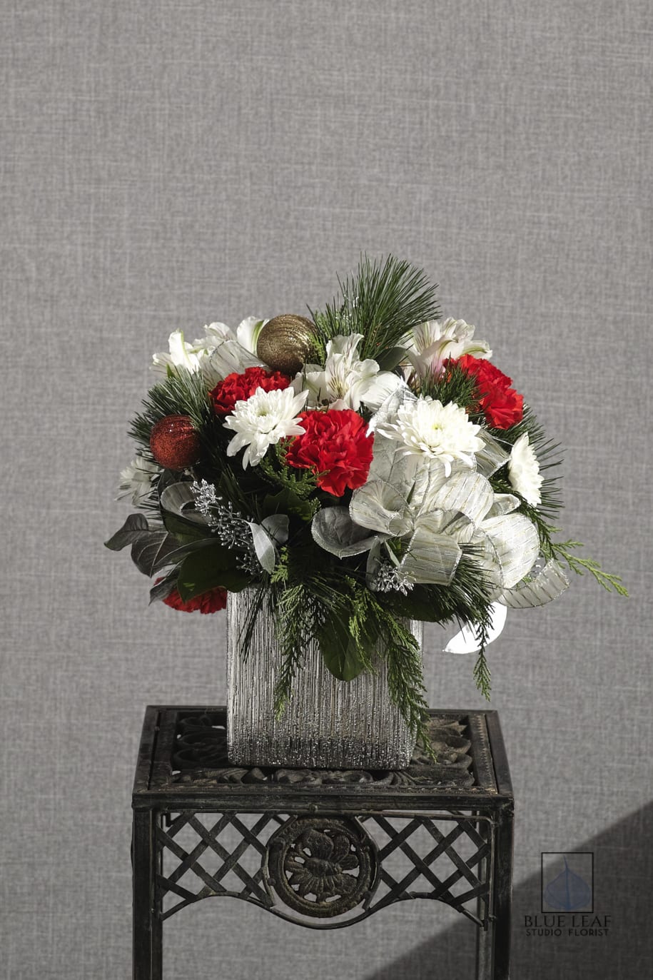 Silver Cube - Arrangement with carnations, mums Silver ribbon etc. The one shown is decorated with Christmas ornaments which will not add unless you would like them add near Christmas. ( just drop us a note in the special instructions area.) This is a blue leaf studio florist design.