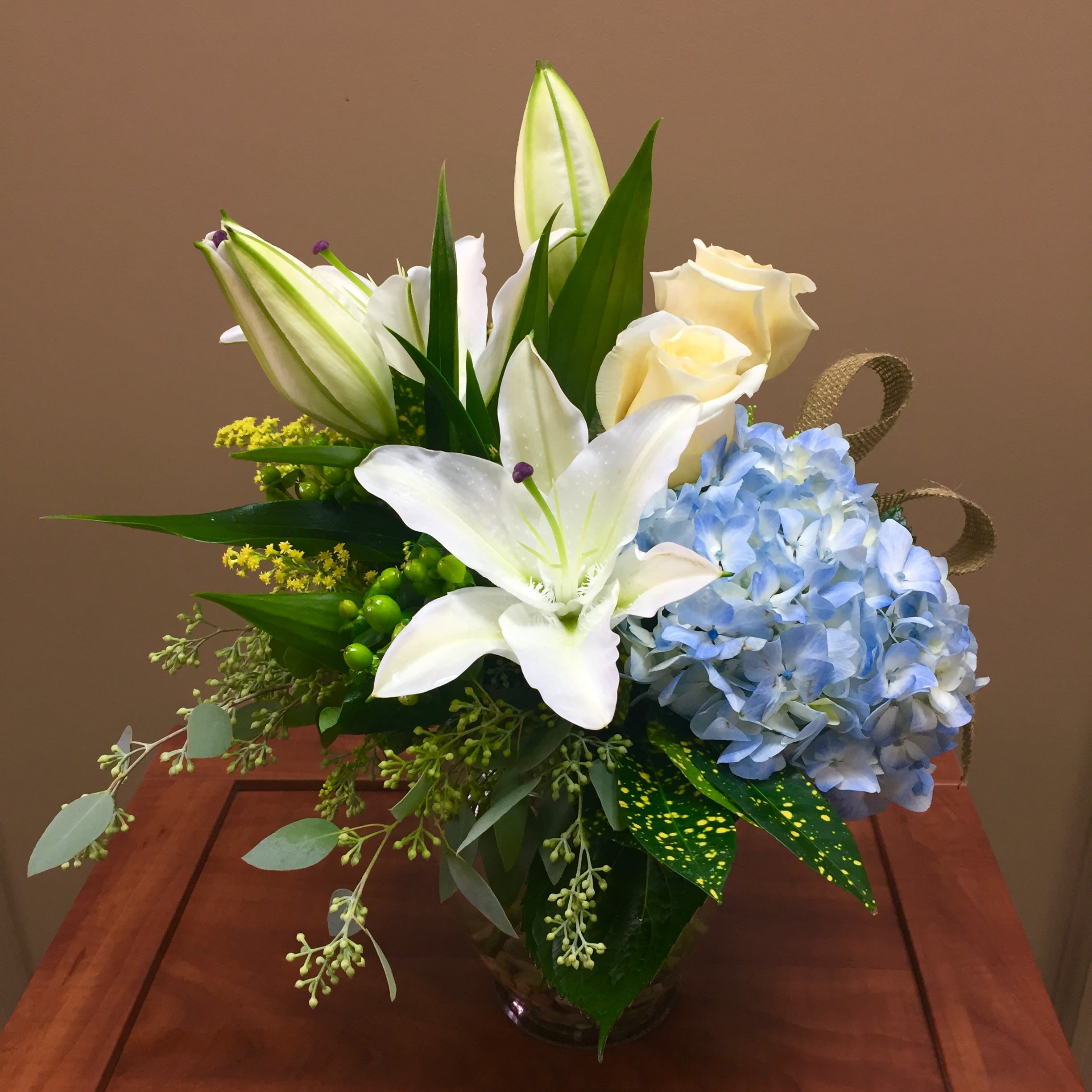 A Day At Moonlight Beach - Ahhhhh...relaxing at the beach....we all need it once in a while. And if we cannot actually make it to the beach, enjoying this beautiful design is the next best thing! Featuring ocean blue hydrangea, fragrant white lilies, crème de la crème roses, sunny yellow solidaster and accents of seeded eucalyptus. Touches of burlap ribbon to top off this beachy look. 