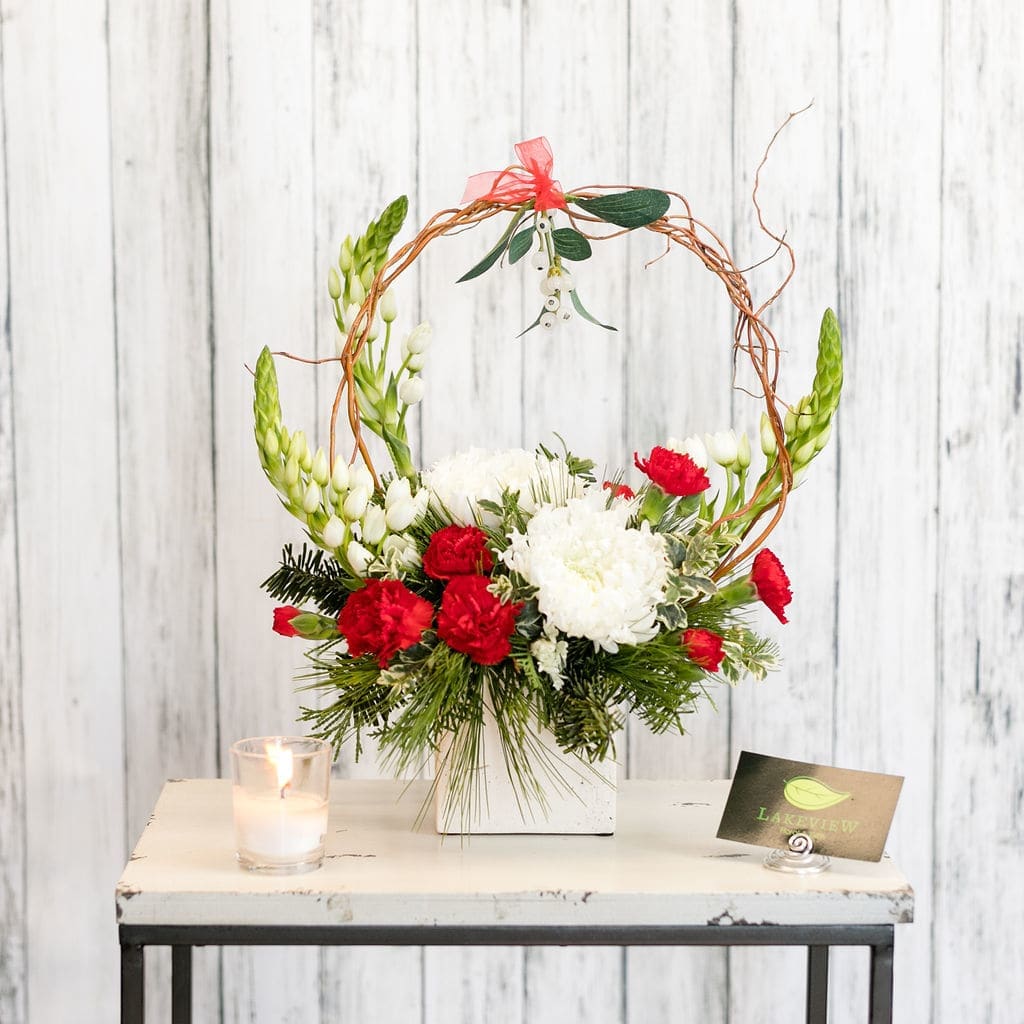 Mistletoe - Let them know (in a not so subtle way) that you'd like to catch them under the mistletoe.  A sprig of faux mistletoe hovers above a holiday collection of red and white blooms.  Perfect for your sweetheart!  Approx: 12&quot;H x 10&quot;W
