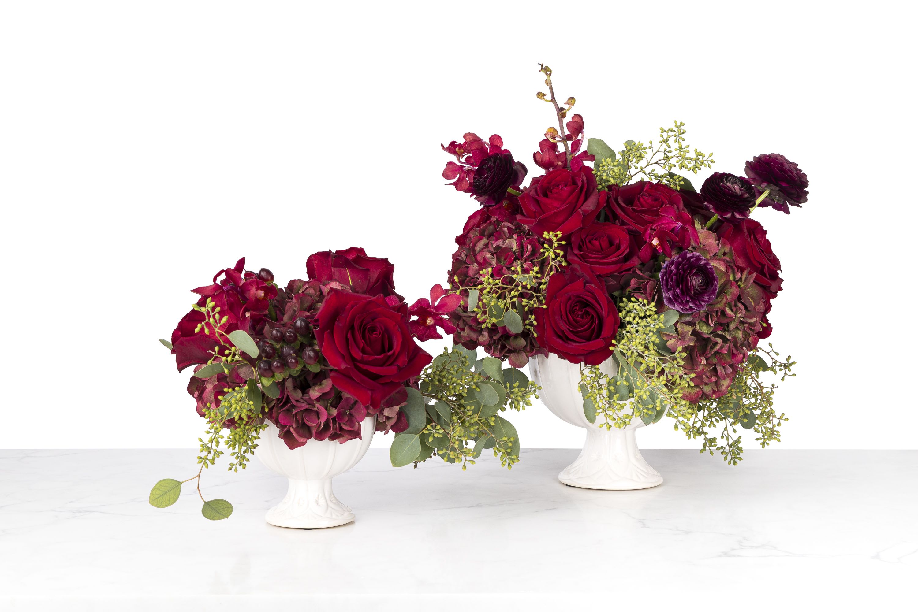 Christmas Elegance - A sophisticated arrangement that works fabulously as part of your holiday decor, or as a show-stopping gift for that special someone on your nice list!  A white embossed ceramic compote filled with antique hydrangeas, exotic orchids, deep red roses and ruby-colored berries.  Standard arrangement is pictured on the left; deluxe arrangement pictured on the right.  Standard arrangement measures approximately 8x8&quot;. Deluxe arrangement measures approximately 11x11&quot;.