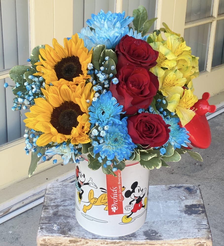 Sunflower Roses Disney Mickey Mouse &amp; Friends Cookie Jar Arrangment  -  Celebrate every moment with a cheerful gift, full of character. Brighten up any room or office with bright yellow sunflowers, red roses, and blue blooms. The lovely arrangement comes displayed in a Disney’s Mickey Mouse &amp; Friends Cookie Jar, which features a classic design and an iconic Mickey Mouse head as the handle. Cookie jar is dishwasher safe and measures 7 ½” x 5”.`