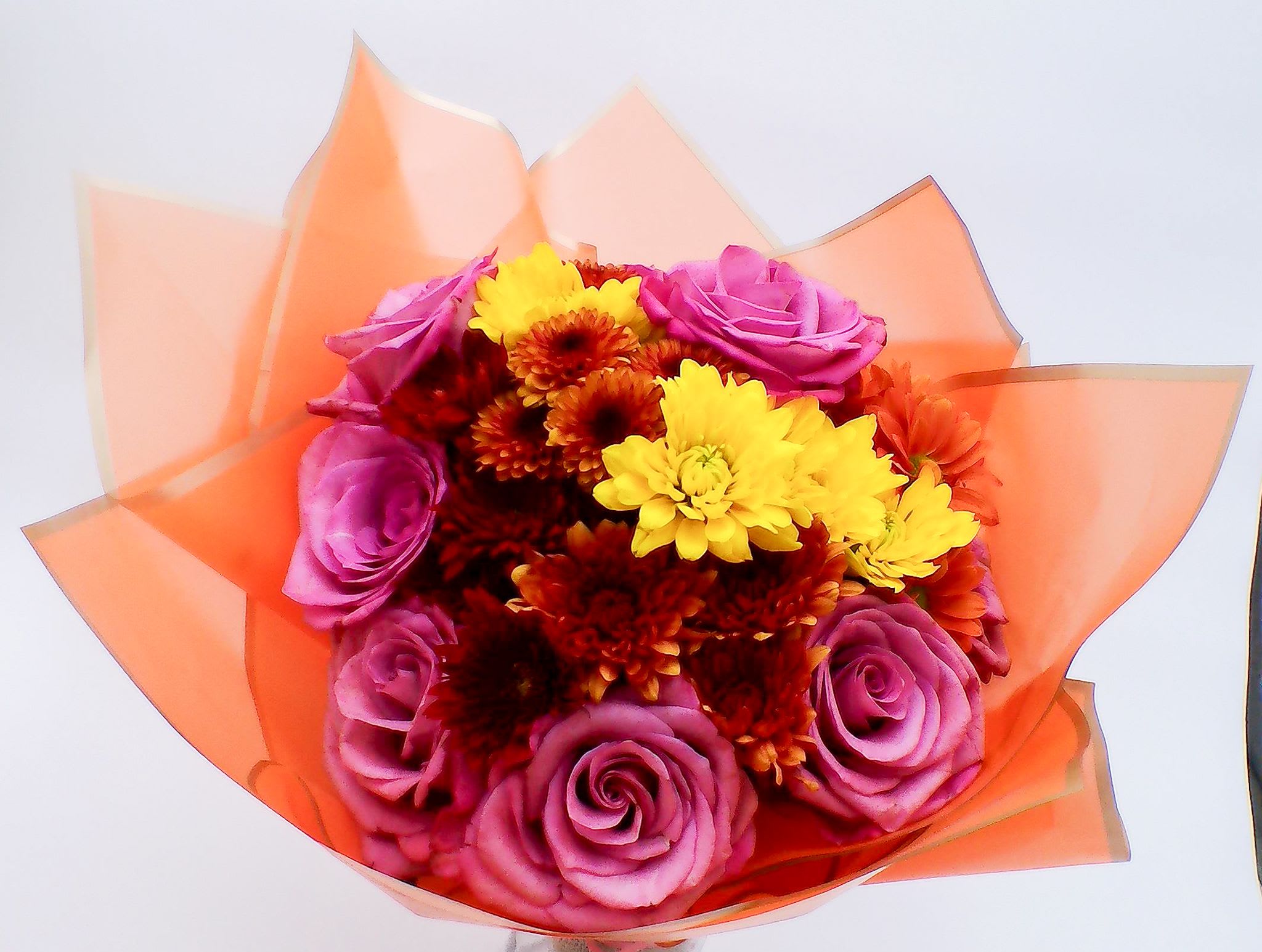 Sunset Glow Bouquet - This radiant Hand-Tied Bouquet is a stunning combination of 6 lavender roses and 6 daisy mums. This bouquet blends elegance with vibrant color for a truly eye-catching presentation.  Wrapped in premium orange floral paper for a warm, celebratory look, this bouquet embodies beauty, gratitude, and affection. Perfect for birthdays, anniversaries, thank-you gifts, congratulations, get-well wishes, just-because surprises, housewarming gifts, and romantic gestures. Total Weight: approximately 350–450 g