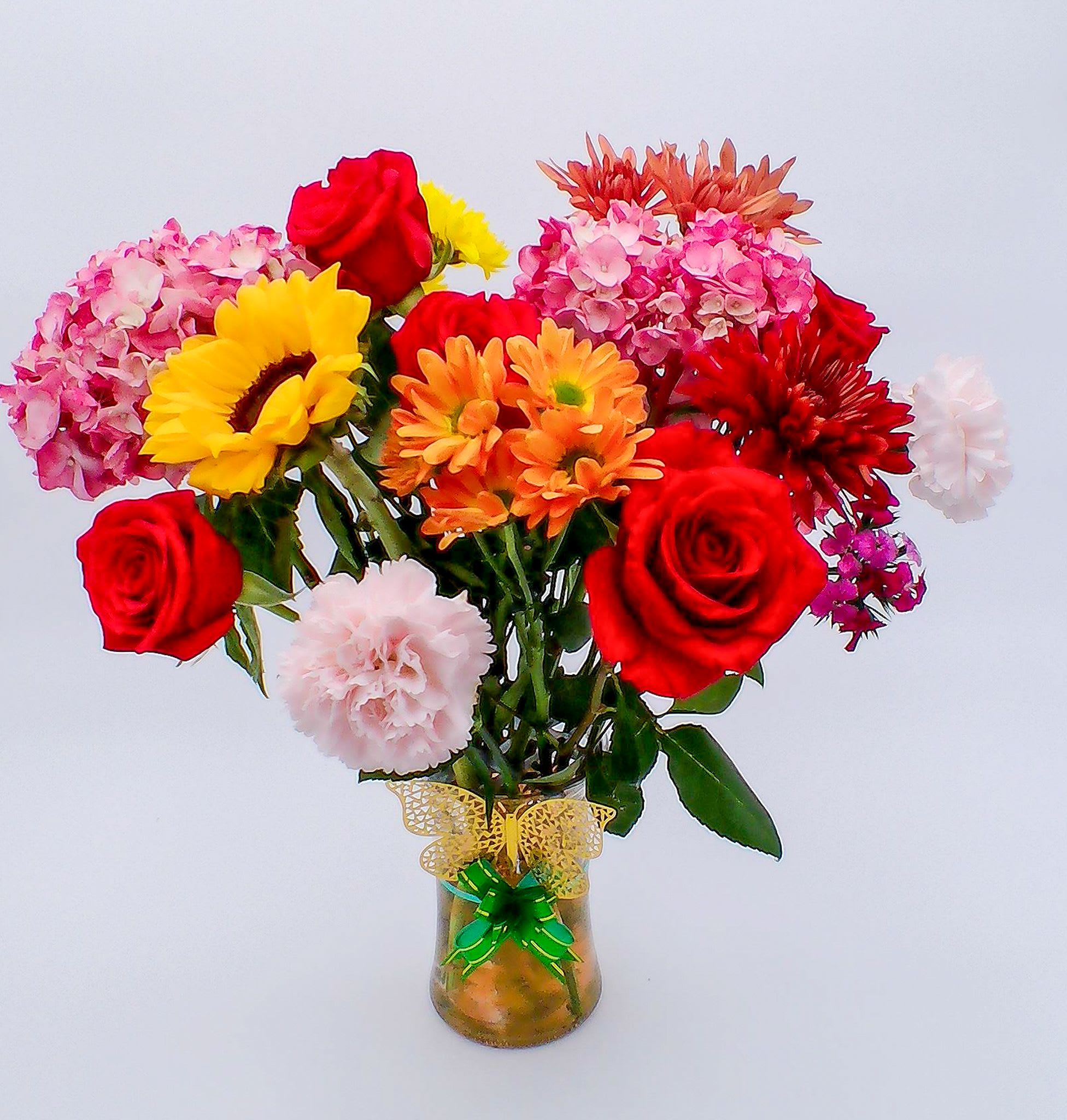 Sunshine  Butterfly Bouquet -  Fresh Flowers Bouquet (18 stems) featuring a joyful blend of roses, gerbera daisies, chrysanthemums, carnations, and hydrangea-style blooms. The bright palette of red, yellow, pink, orange, and soft blush tones creates a warm, uplifting display perfect for any celebration. Clear glass vase with decorative ribbon Weight: Approximately 450–550 g Ideal for: birthdays, congratulations, thank-you moments, get well soon wishes, anniversaries, just-because surprises