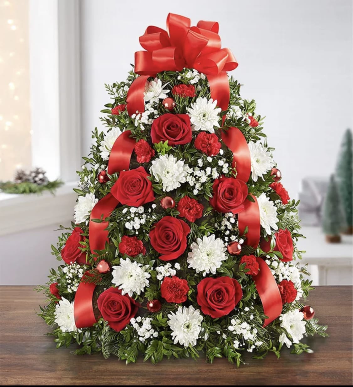 Holiday Flower Tree - The holiday favorite that started it all! Our flower tree arrangement is popular for its festive style and compact size, which fits perfectly into any space. Gathered with fragrant evergreens, then trimmed with decorative ornaments and a merry red bow on top, this floral twist on a traditional tree makes a truly original gift for family, friends or your own home