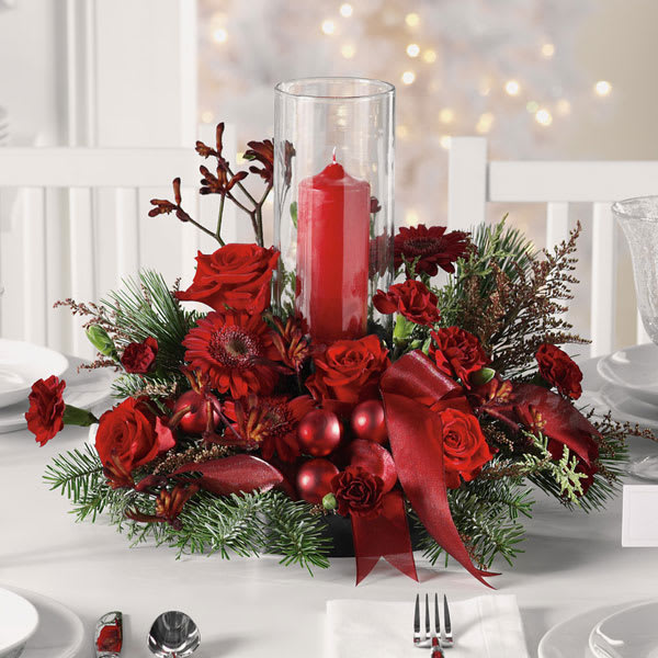 All Red Holiday Centerpiece - Set the holiday table with a traditional favorite! Fresh and fragrant Christmas greens create a fragrant base for the rich red roses and carnations in our merry red centerpiece. Accented with berries, red ornaments and ribbon, this classic arrangement comes with a hurricane vase and pillar candle to create a warm and cozy atmosphere for your Christmas celebration.