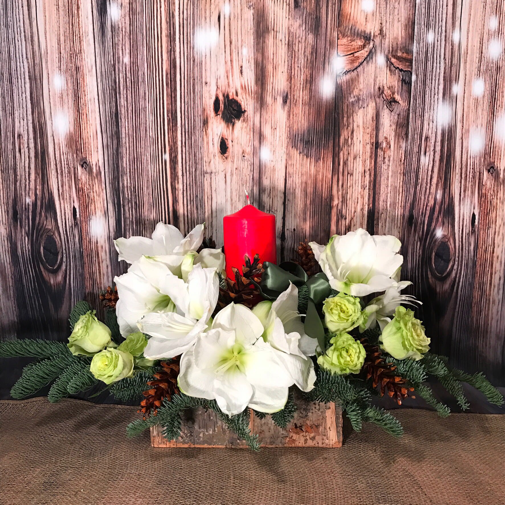 HOLY CANDLE CENTERPIECE  - OBLONG CENTERPIECE IN NATURAL BIRCH BASKET MIX CHRISTMAS GREENS, WHITE AMARRILYS, GREEN APPLE ROSES AND CLUSTERS OF PINE CONES.