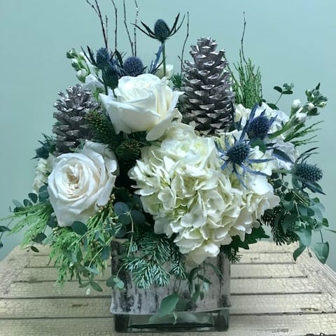 White Birch CR48 - Celebrate the season with this arrangement in cool shades of white, blue and silver.  This large cube arrangement is overflowing with white hydrangea, blue thistle, white spray roses, silver pine cones and sparkling birch branches.  It's the perfect way to say happy holidays!